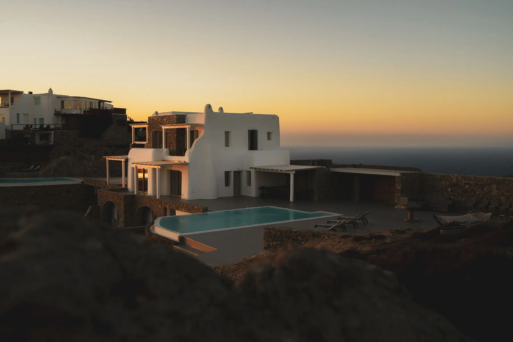 A white seaside building beside a swimming pool at sunset.