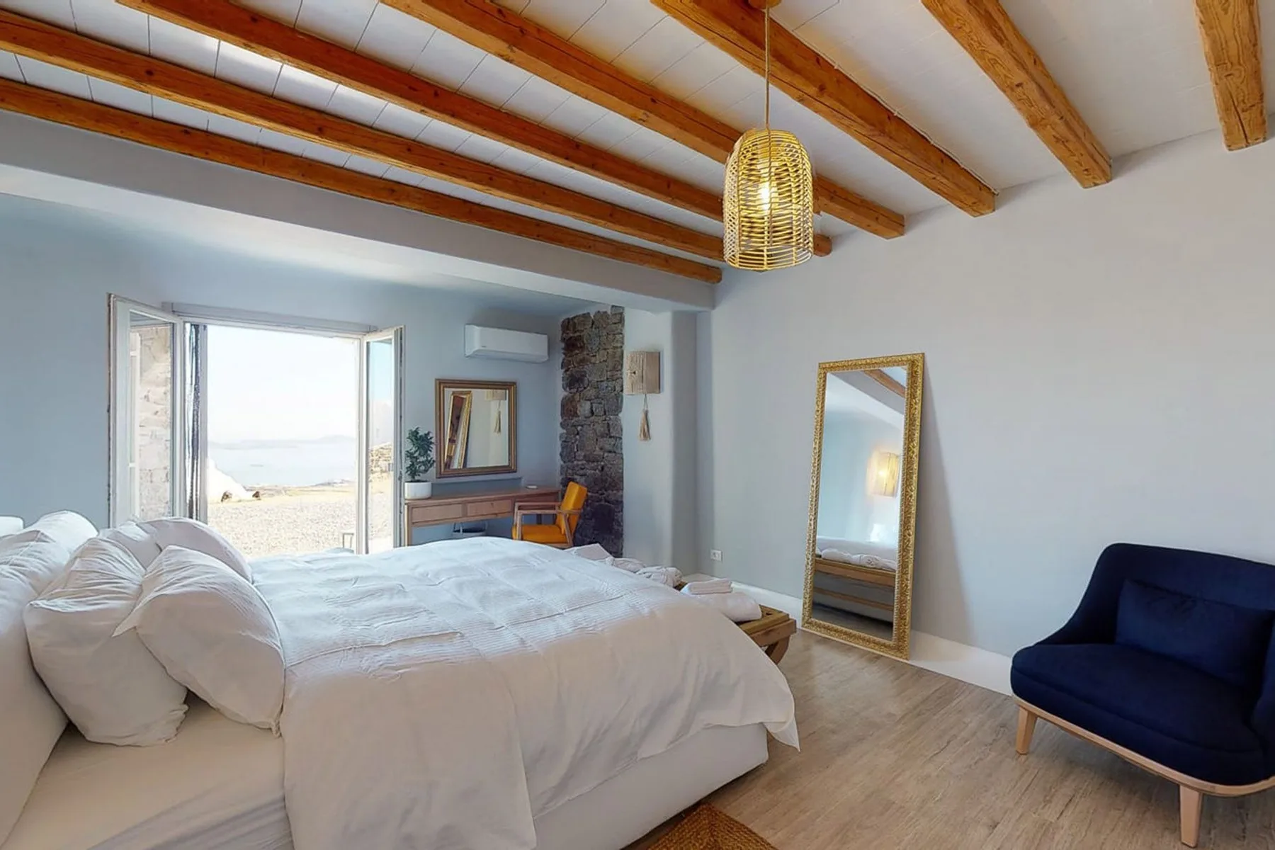 A bedroom with a large bed, exposed ceiling beams, and a glass door opening outside.