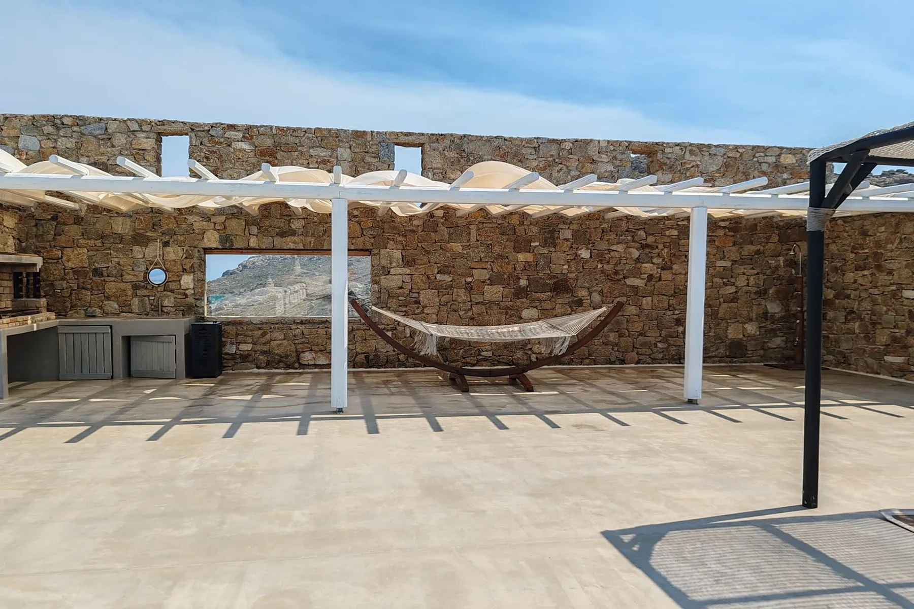 A shaded outdoor patio with a hammock between stone walls.