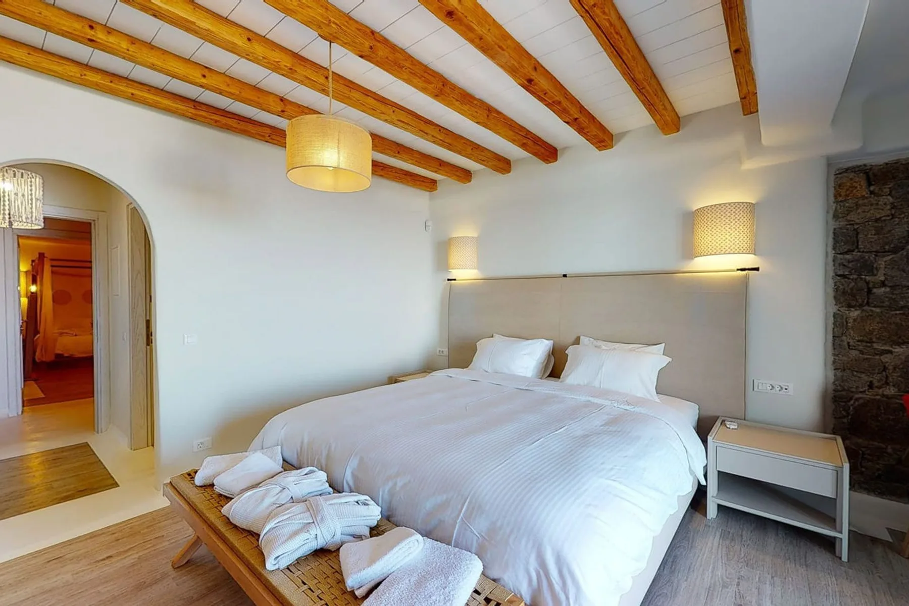 A bedroom with a large bed beneath exposed wooden ceiling beams.