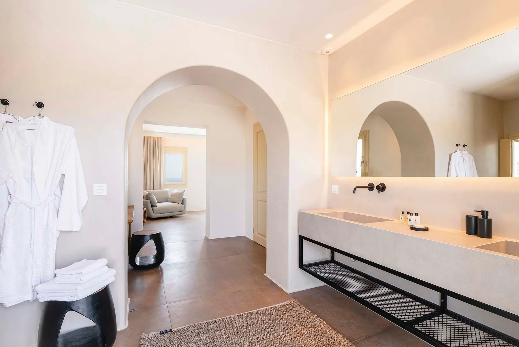 A bright bathroom with a long vanity, large mirror, and an arched doorway.