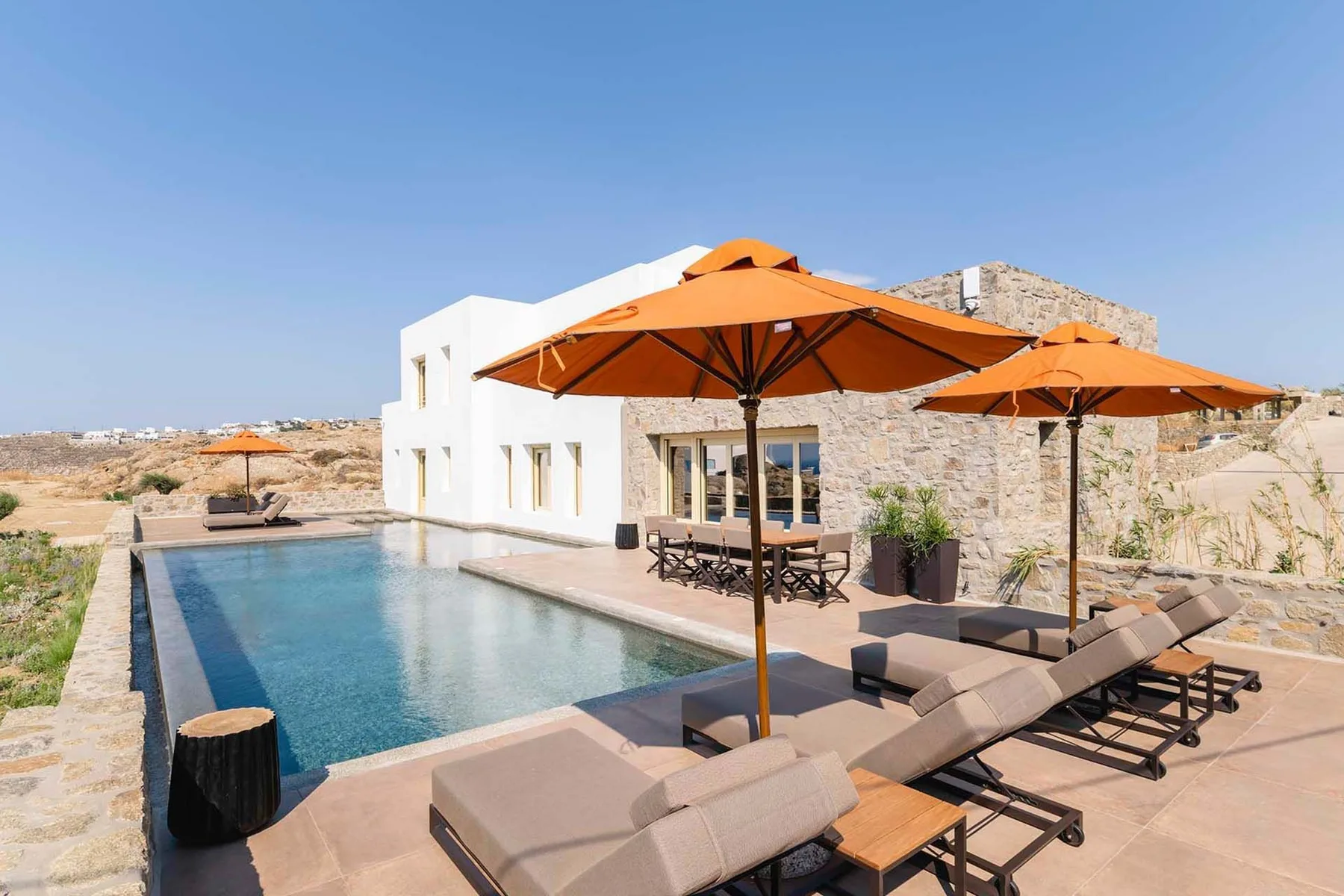 An outdoor pool area with sun loungers and orange shade umbrellas.