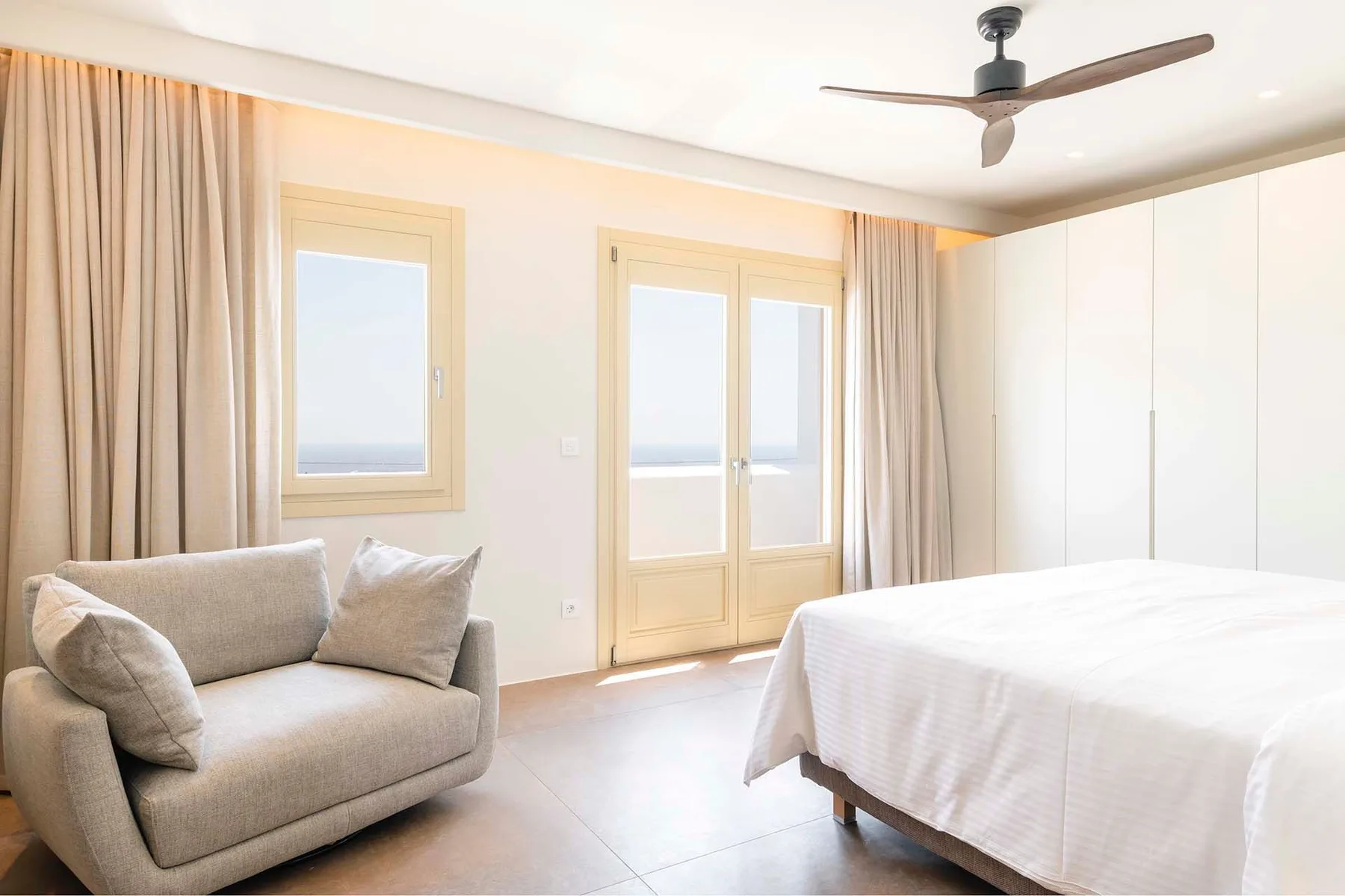 A bright bedroom with a bed, seating, and glass doors opening to a balcony.