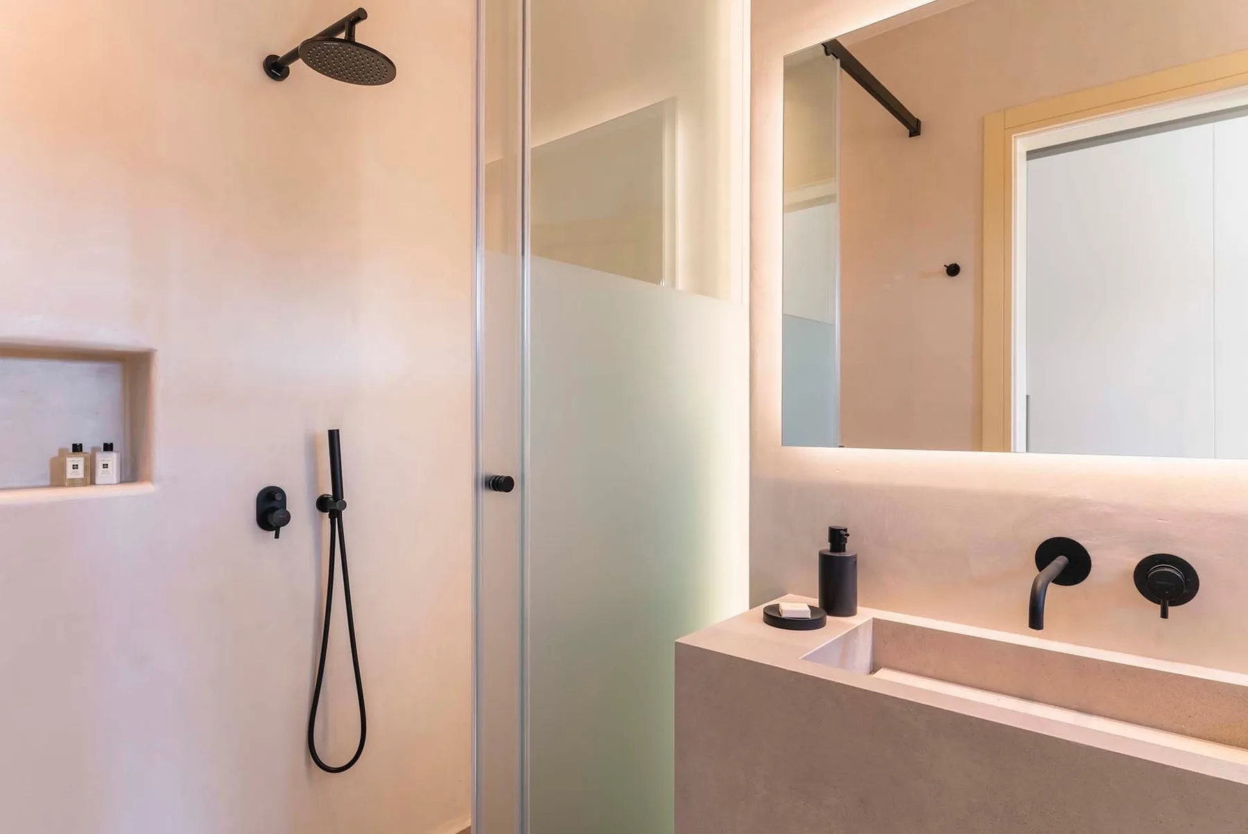 A bathroom with a glass shower, wall-mounted shower fixtures, and a sink.