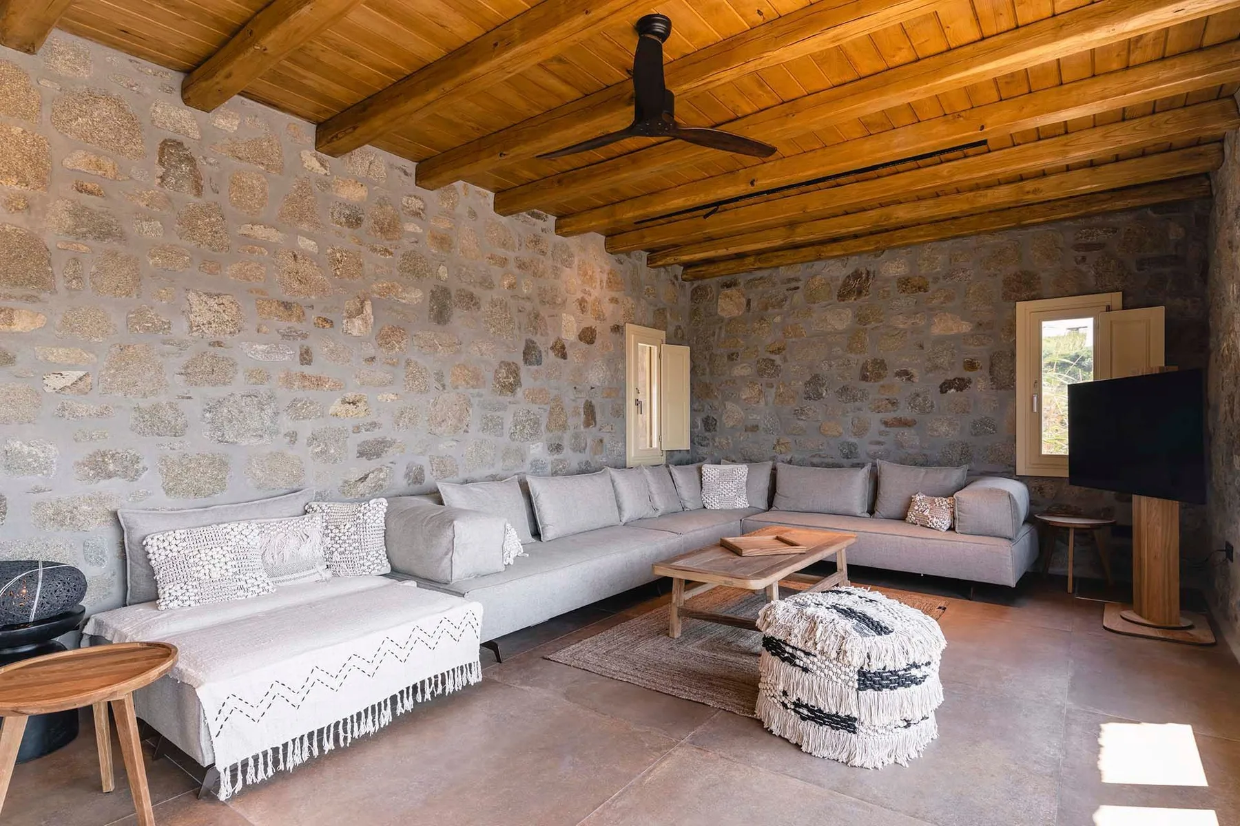 A living room with stone walls, wooden ceiling beams, and sectional seating.