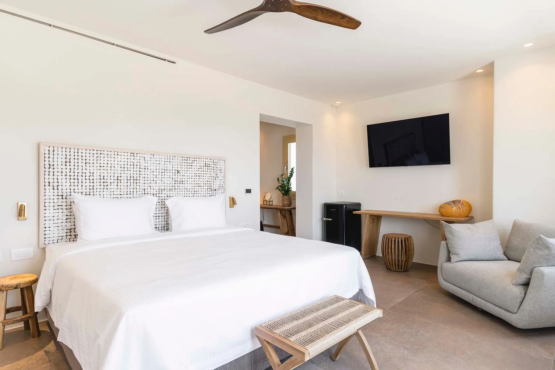A bright bedroom with a large bed, wall-mounted television, and seating.