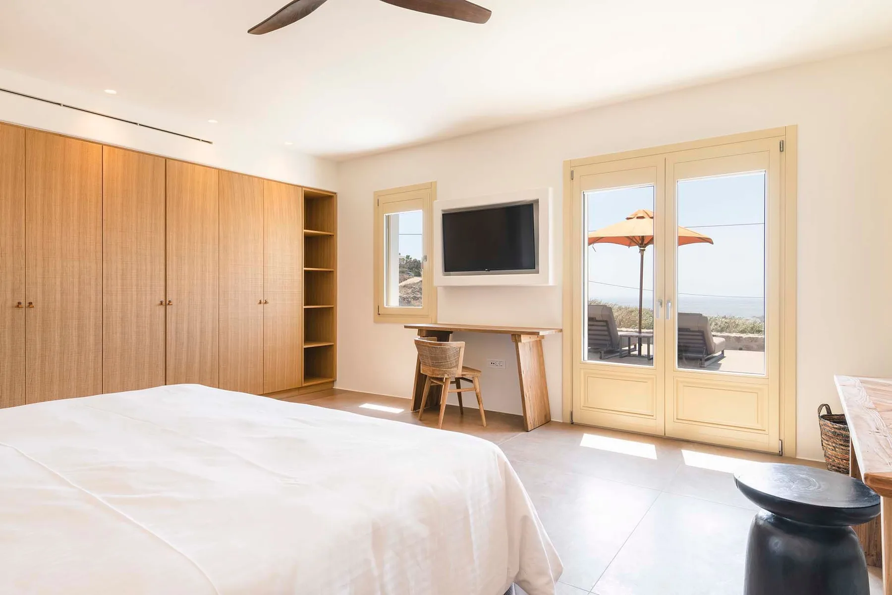 A bright bedroom with a large bed, built-in storage, and glass doors opening to a patio.
