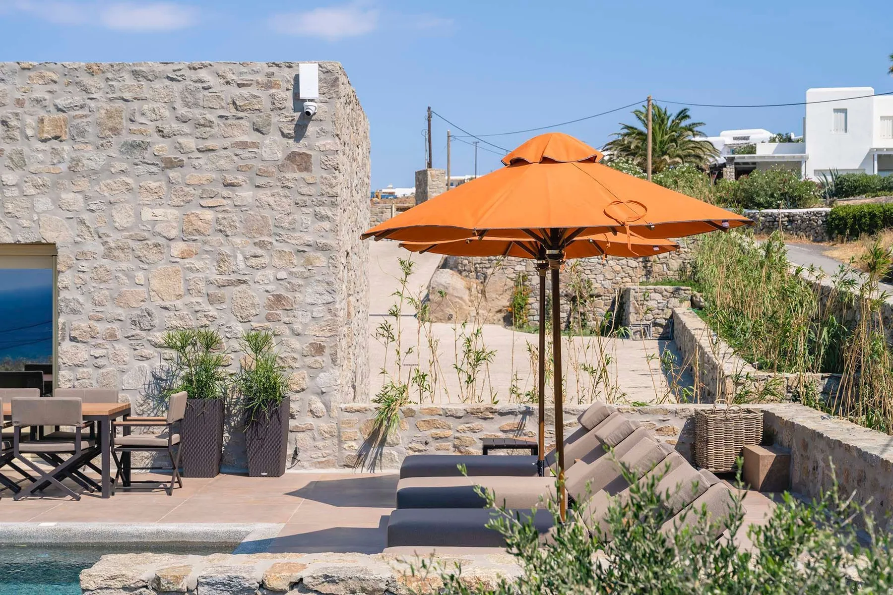 A stone patio with an orange umbrella and outdoor seating.