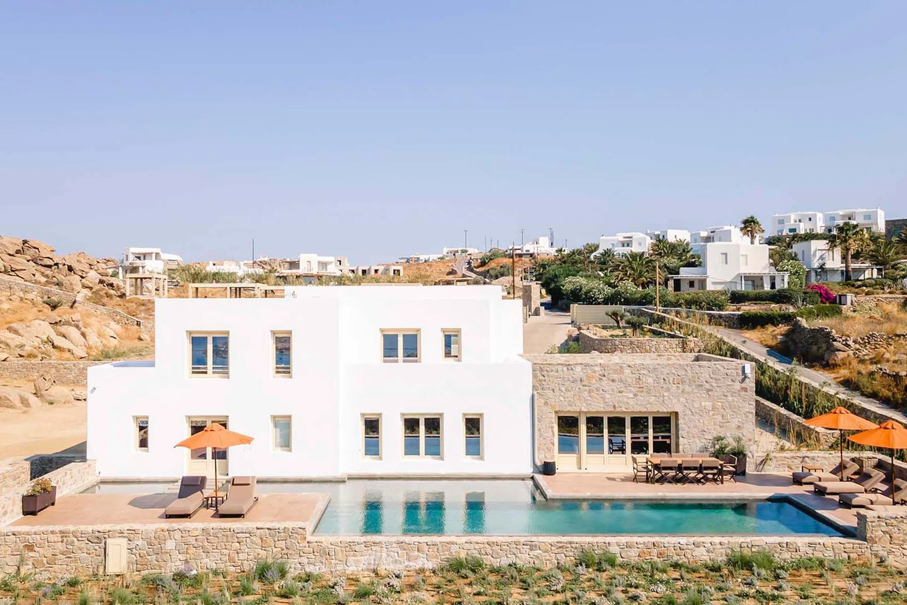 A white villa beside a swimming pool, with hillside homes in the background.