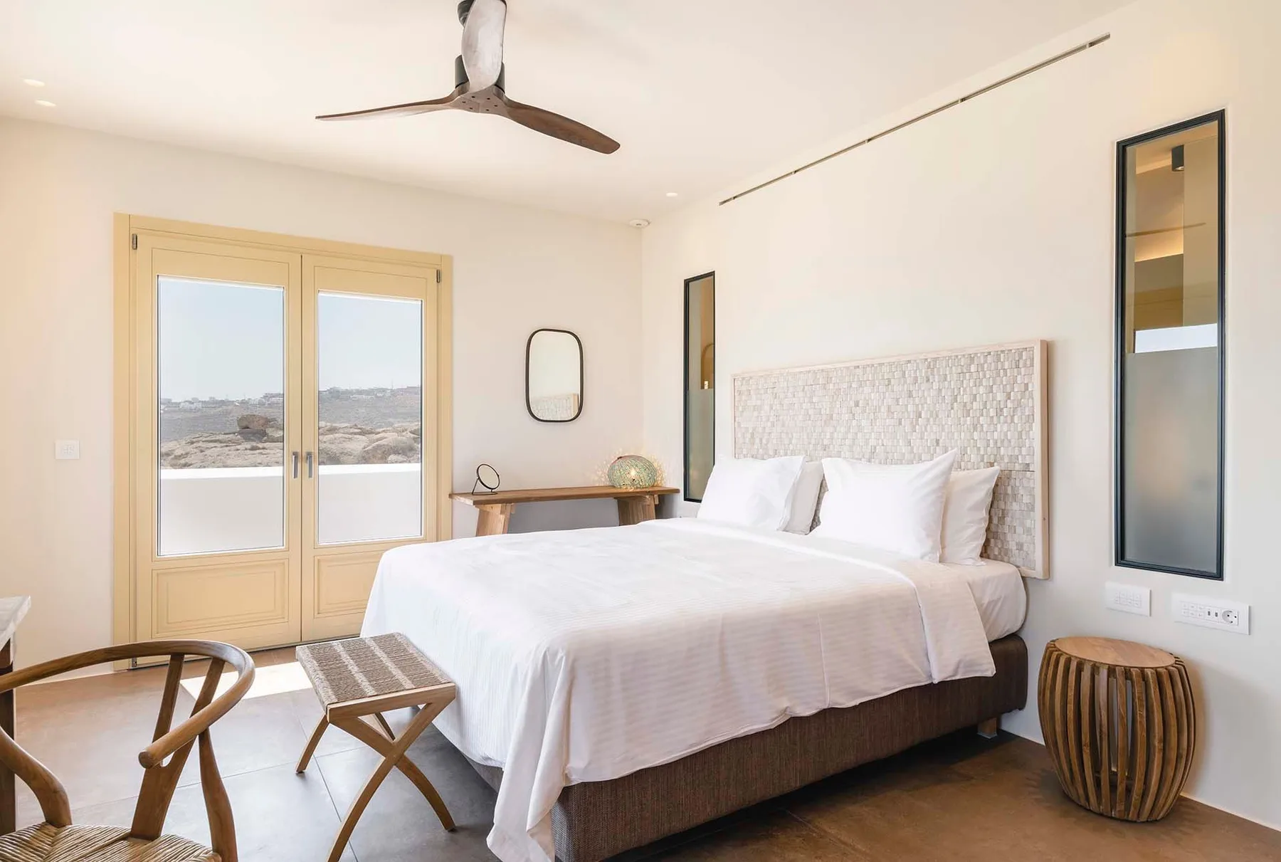 A bright bedroom with a neatly made bed and glass doors overlooking the landscape.