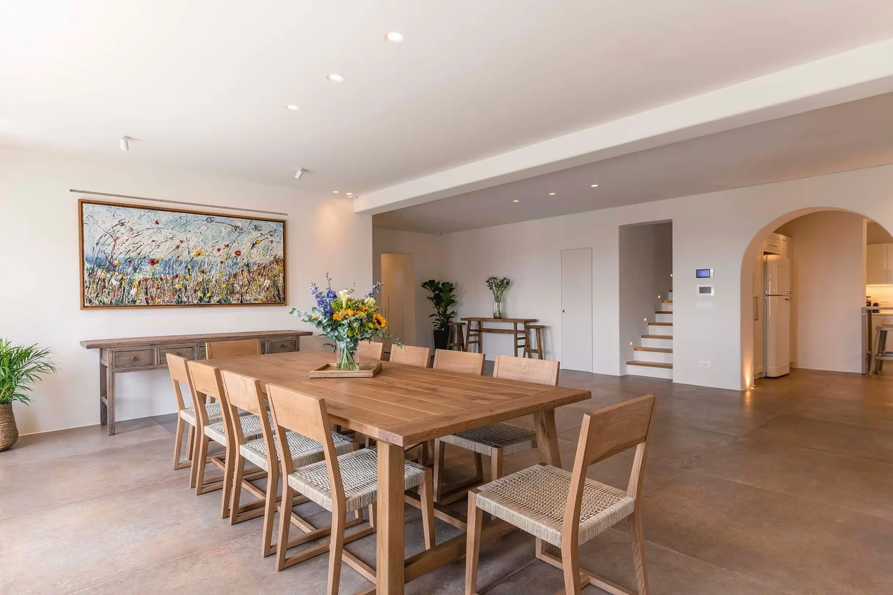 A bright dining area with a long wooden table, seating, and colorful wall art.