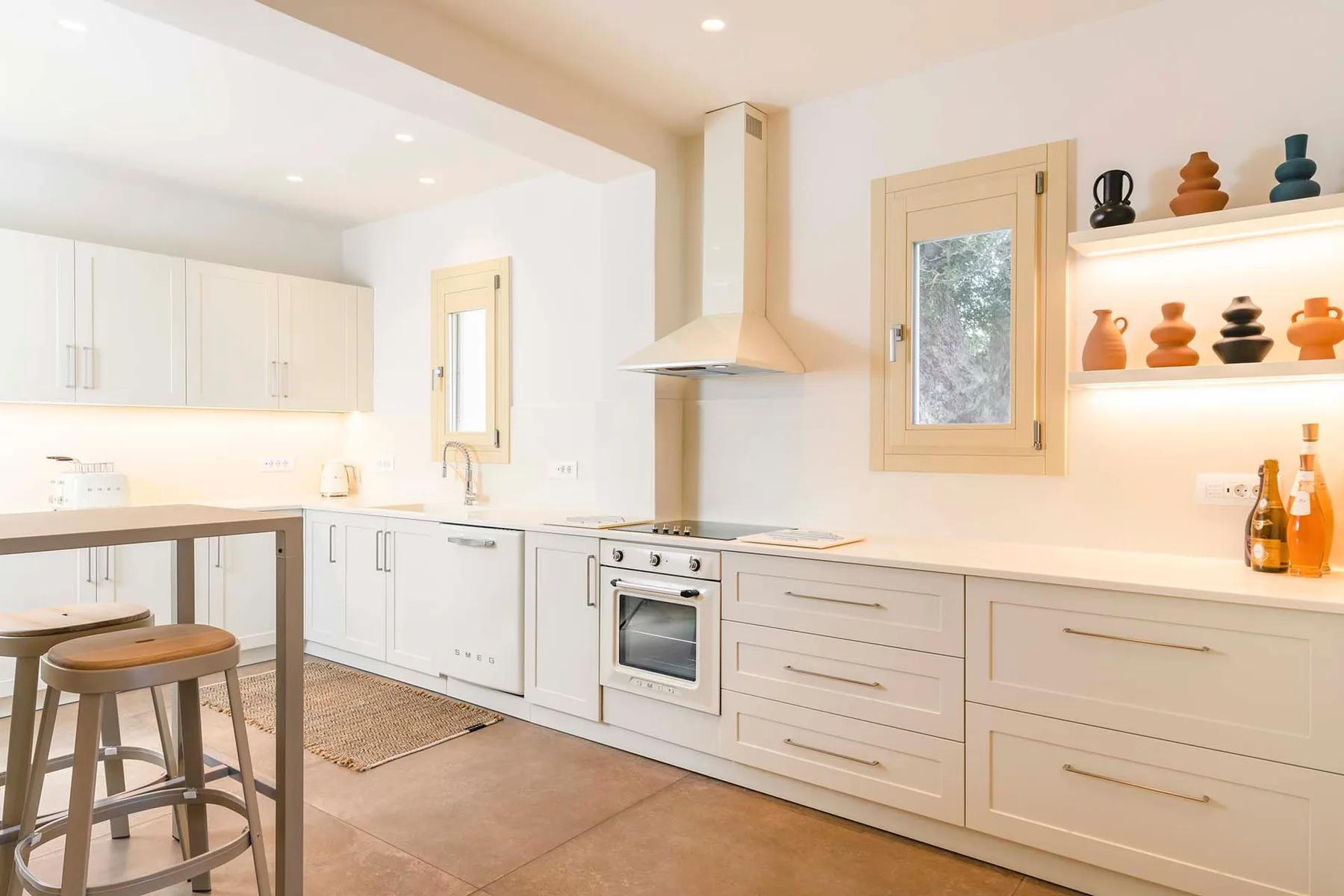A bright white kitchen with a cooking range, sink, and built-in shelves.