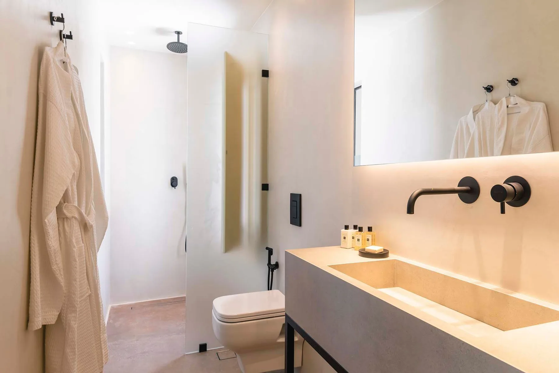 A bright bathroom with a walk-in shower, toilet, and long vanity.
