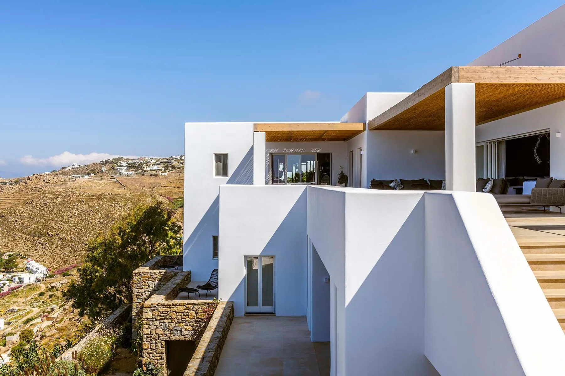 A modern white building has a terrace overlooking a dry, hilly landscape.