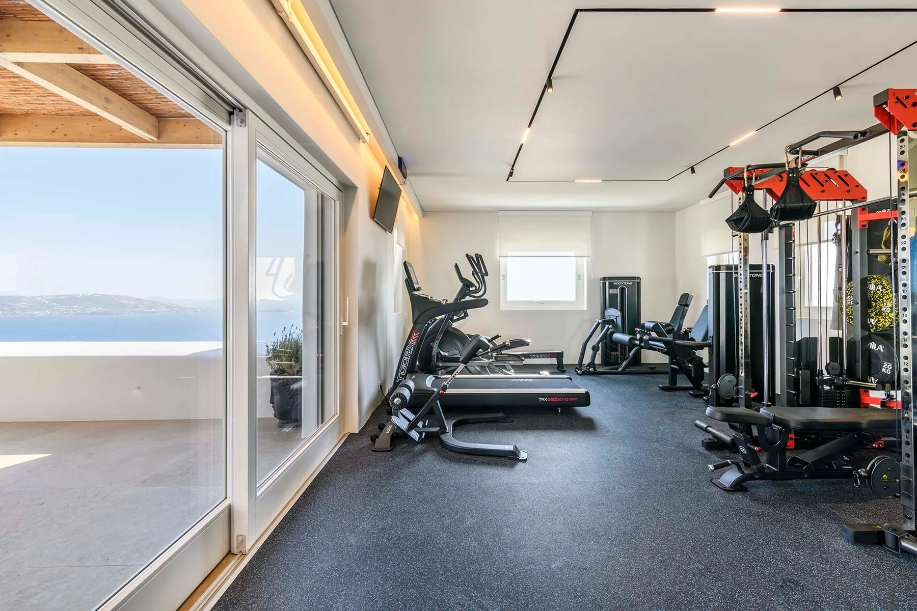 A gym with exercise equipment and large windows overlooking the water.