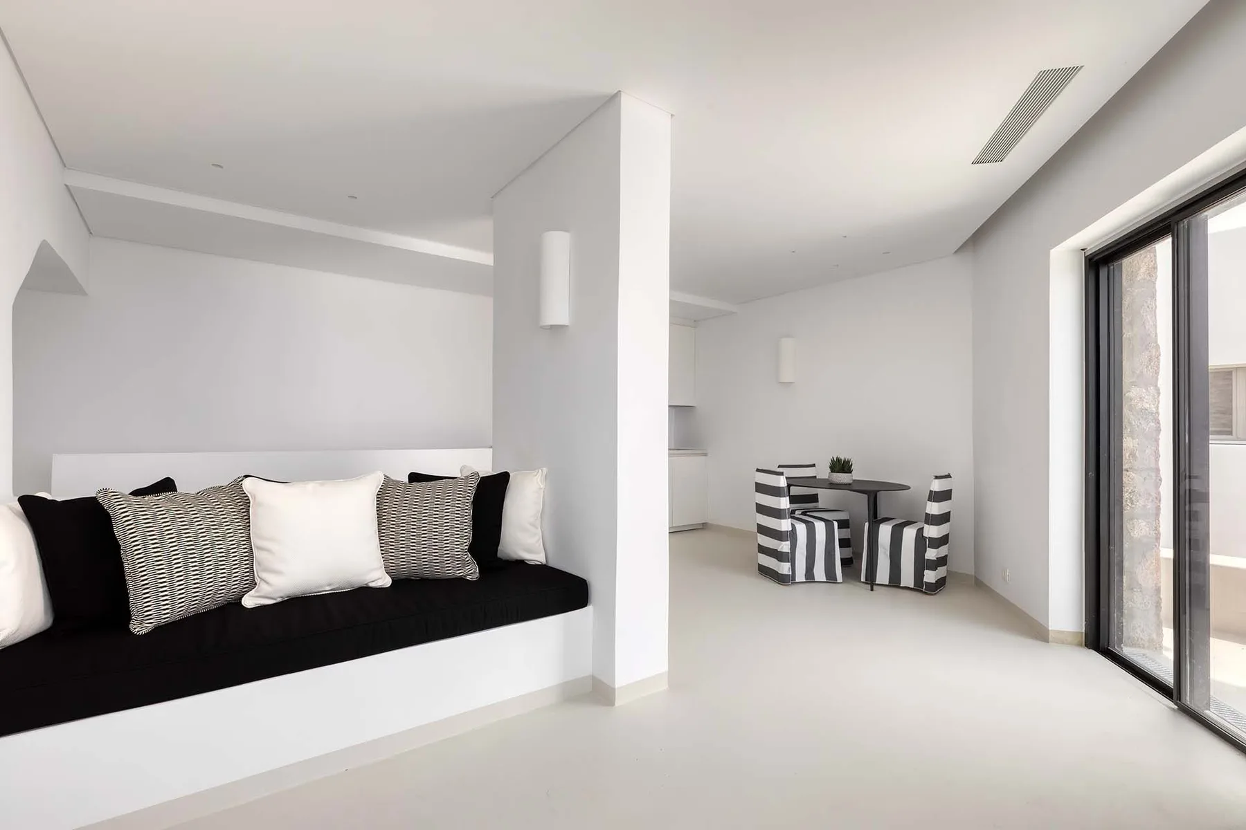A bright white living area with a cushioned bench and a small dining table.