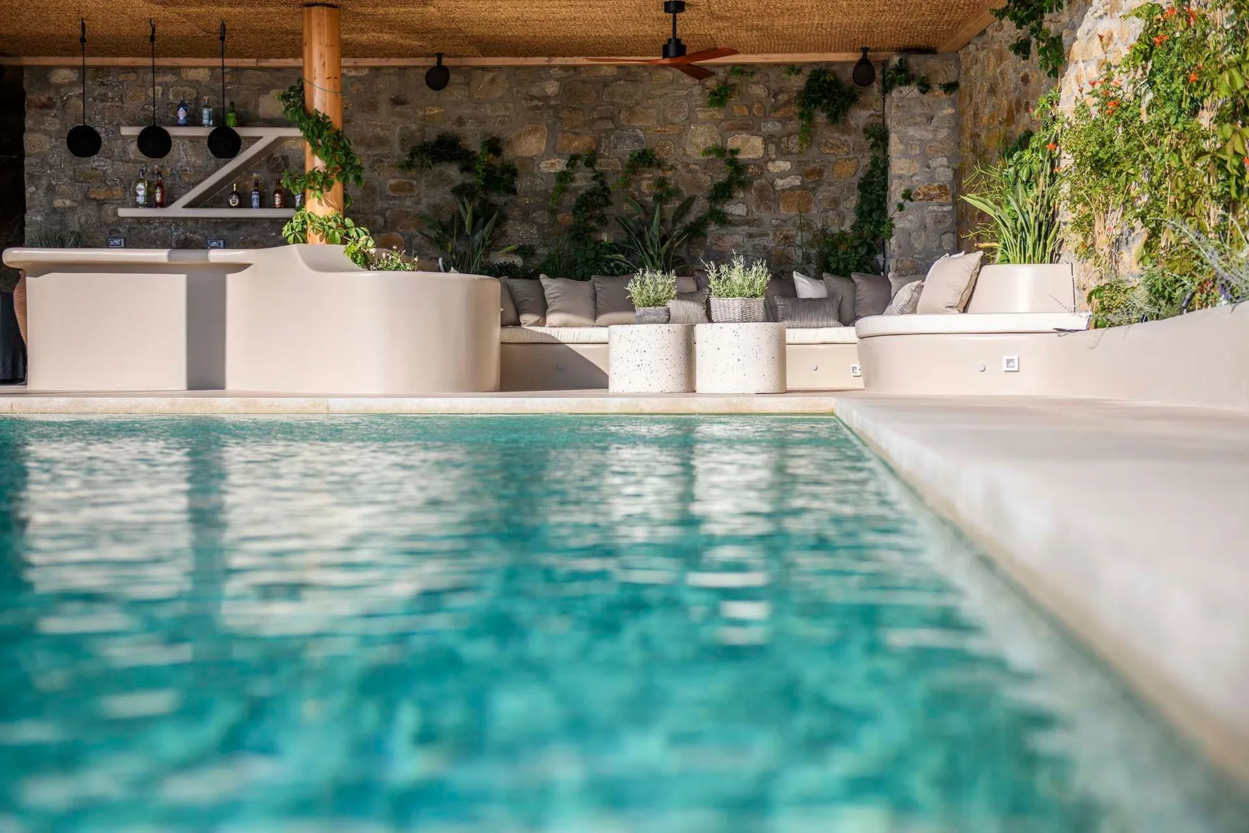 A swimming pool beside a lounge area with pale seating and plants.