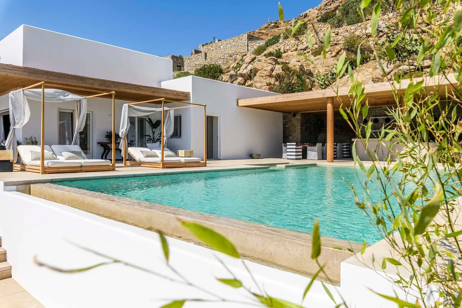 A modern villa opens onto a swimming pool, with shaded seating beside the water.