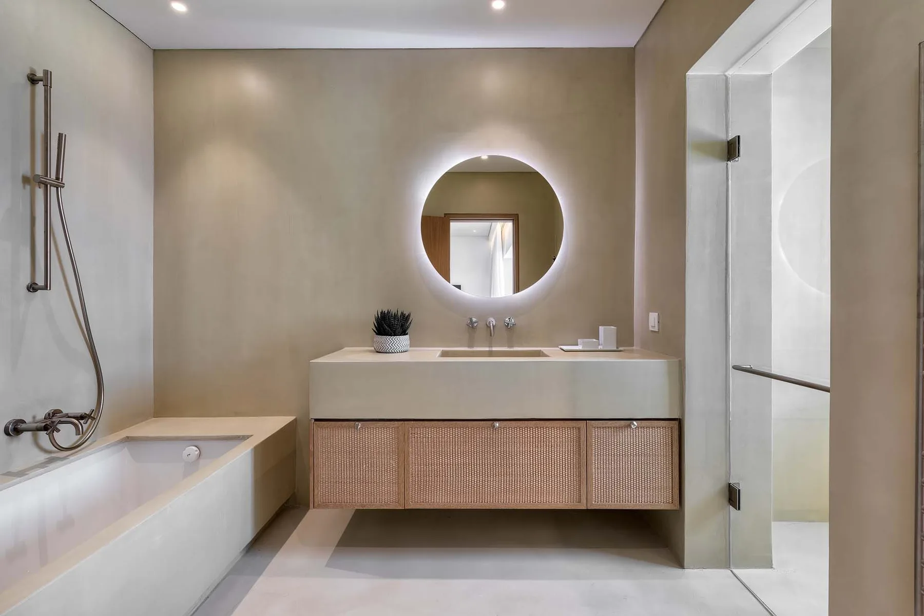 A modern bathroom with a bathtub, vanity, and round mirror.
