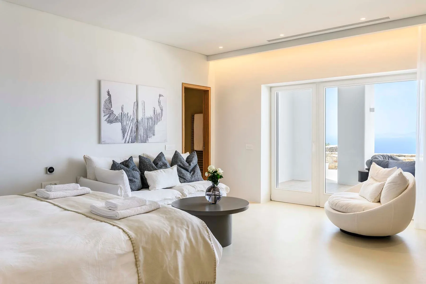 A bright bedroom with a bed, seating, and glass doors opening to a balcony.