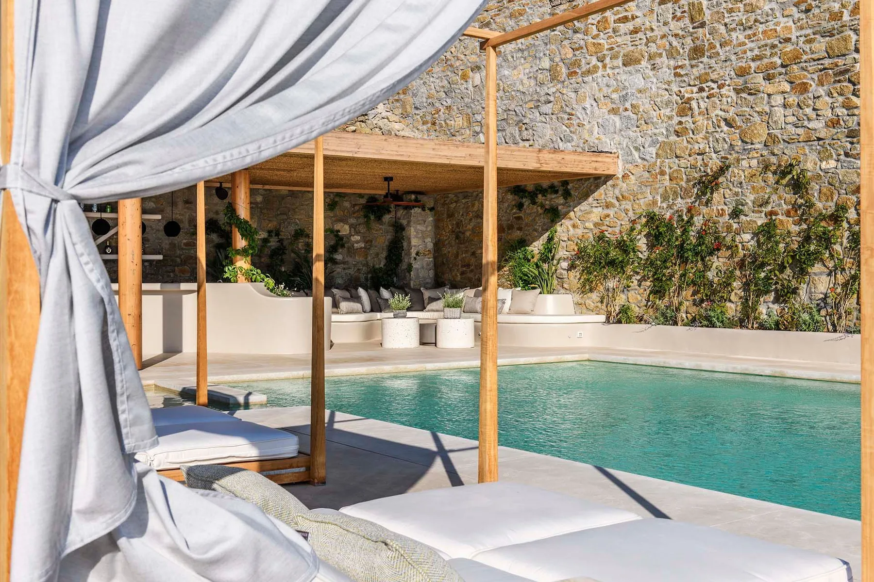 A courtyard pool beside a stone wall, with shaded seating under a canopy.