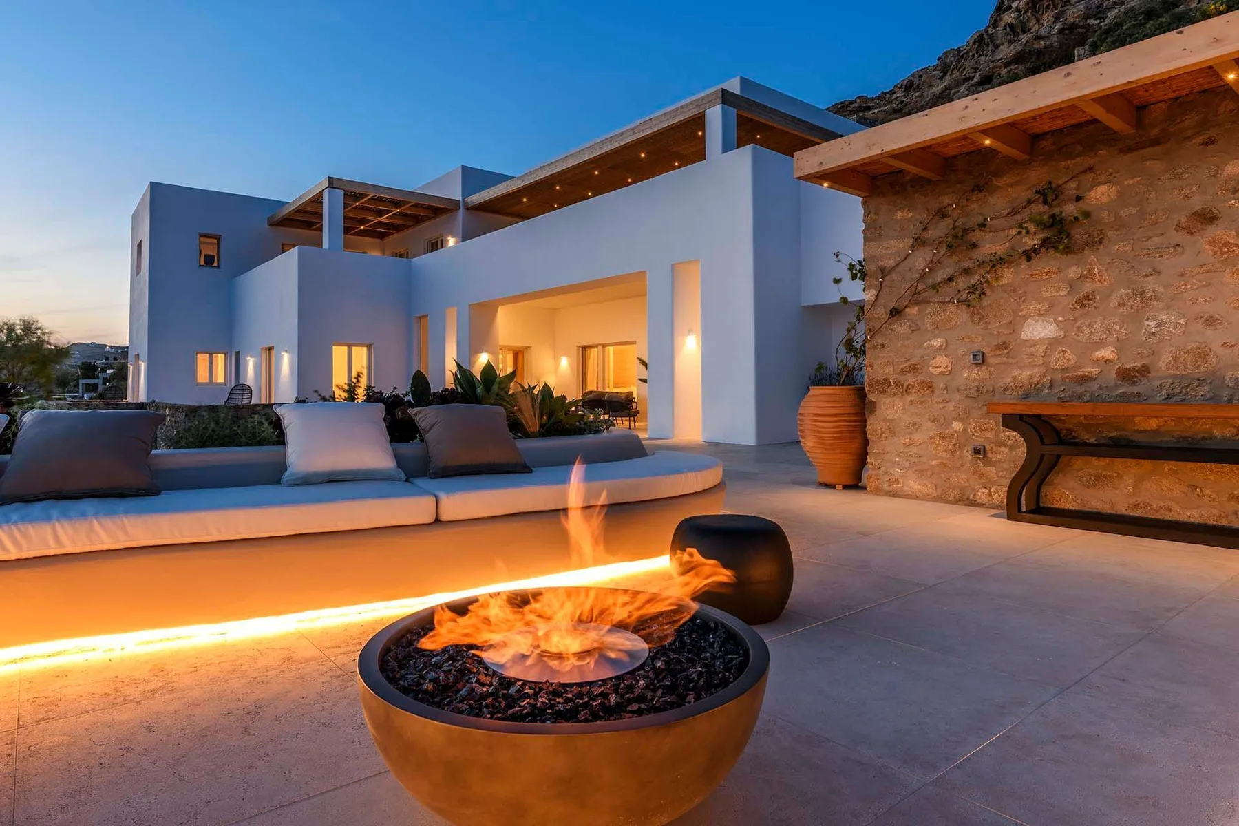 A modern outdoor patio features lounge seating and a lit fire pit.