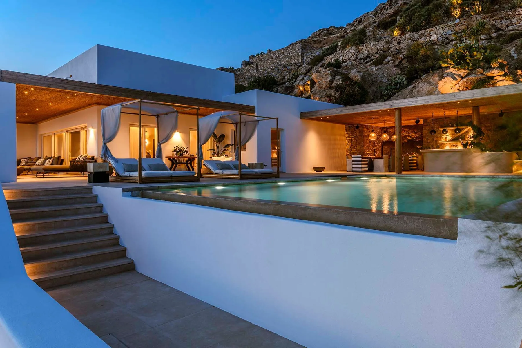A modern villa terrace overlooks an illuminated swimming pool and outdoor seating area.