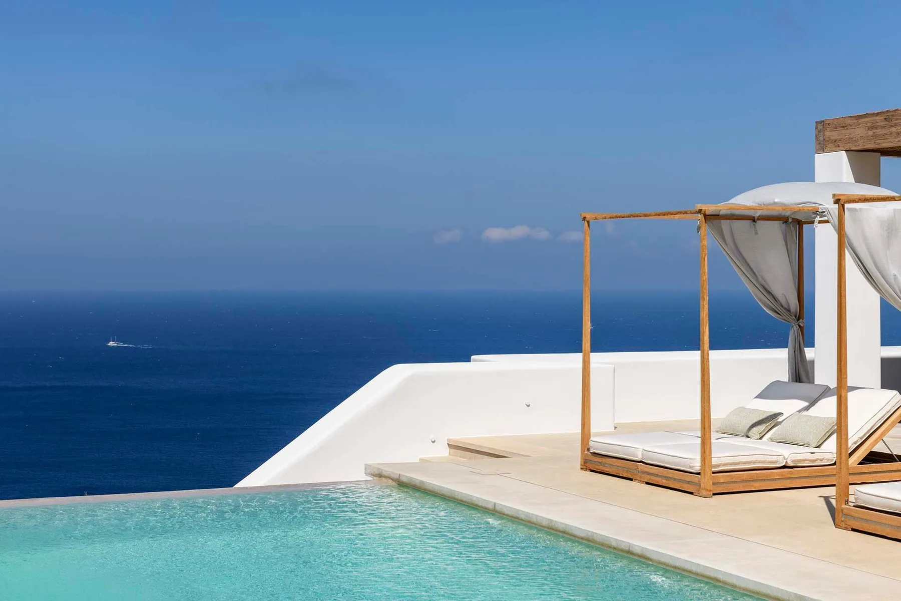 A rooftop pool overlooks the sea, with a shaded daybed on the deck.