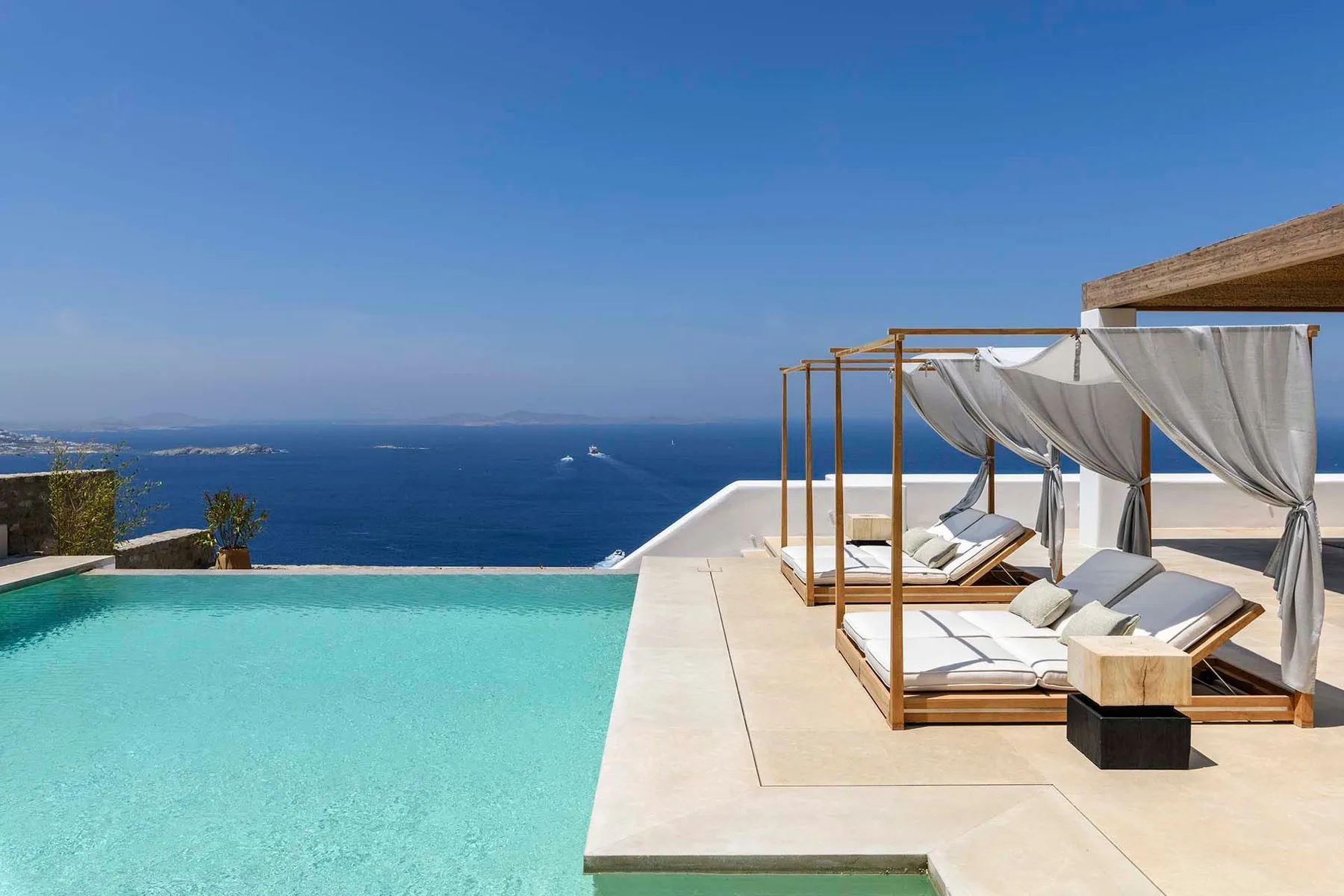 An infinity pool overlooks the sea beside shaded lounge seating.