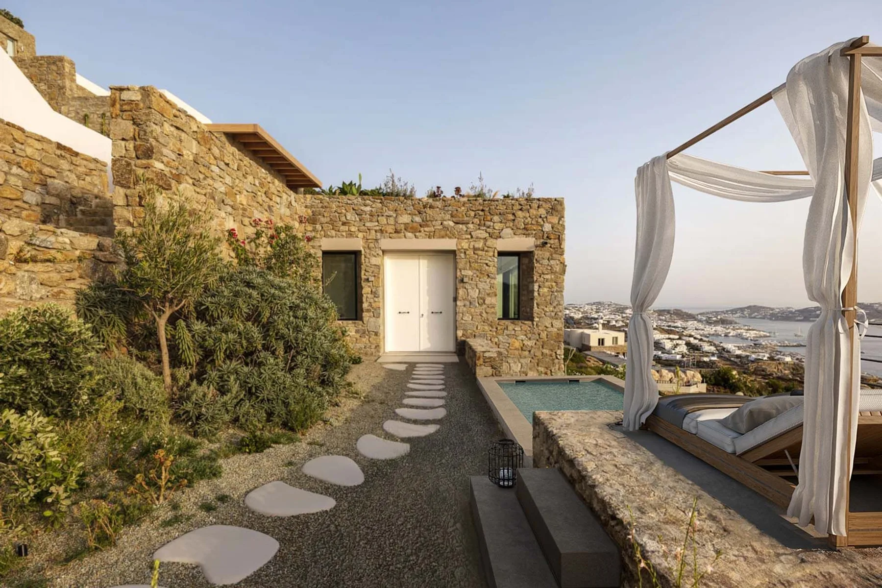A stone exterior patio has a stepping-stone path and a curtained daybed overlooking the town.