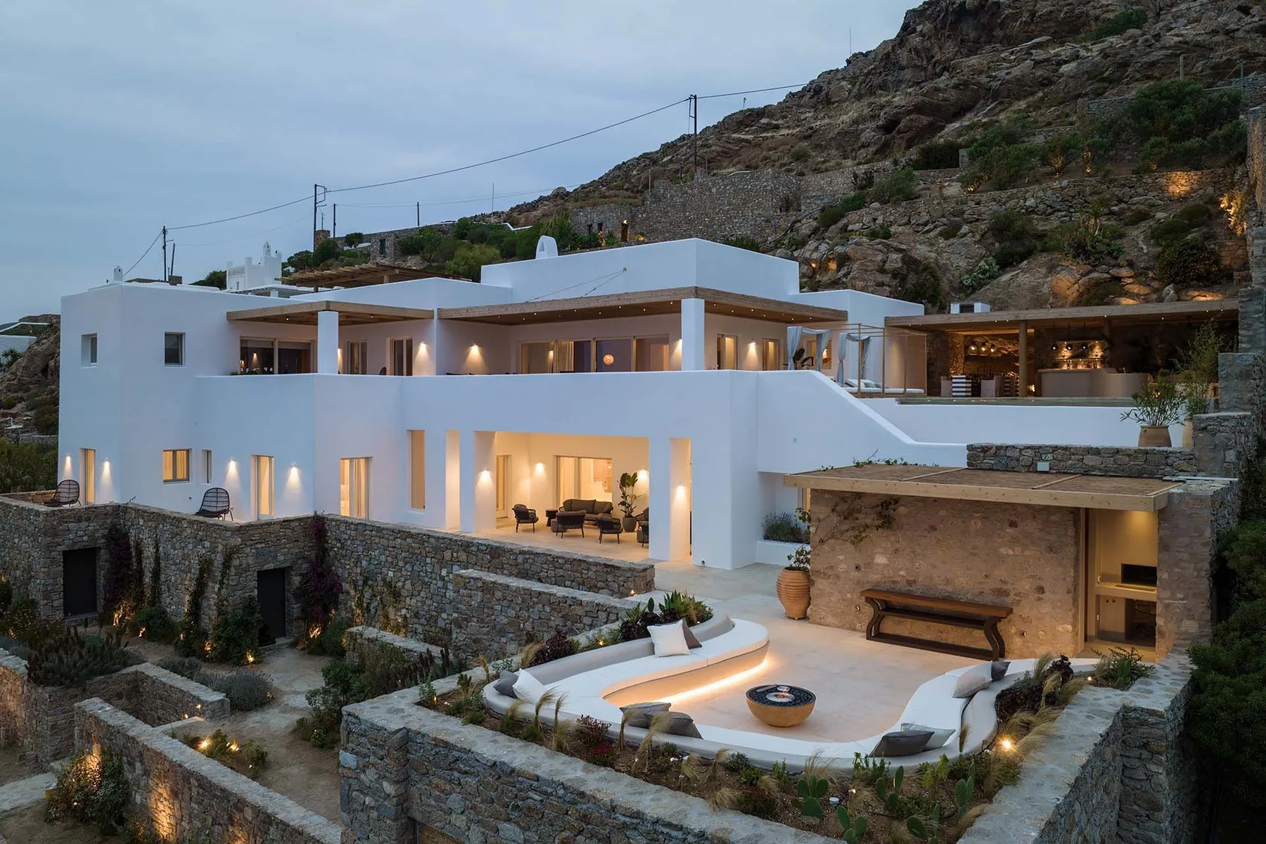 A modern hillside villa with an illuminated outdoor terrace and seating area.