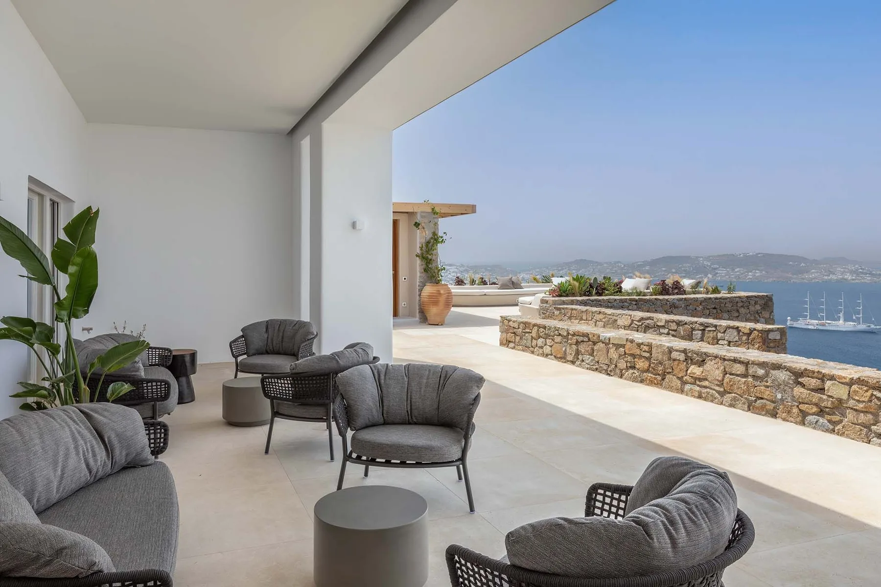 An open-air terrace seating area overlooks the sea and distant coastline.