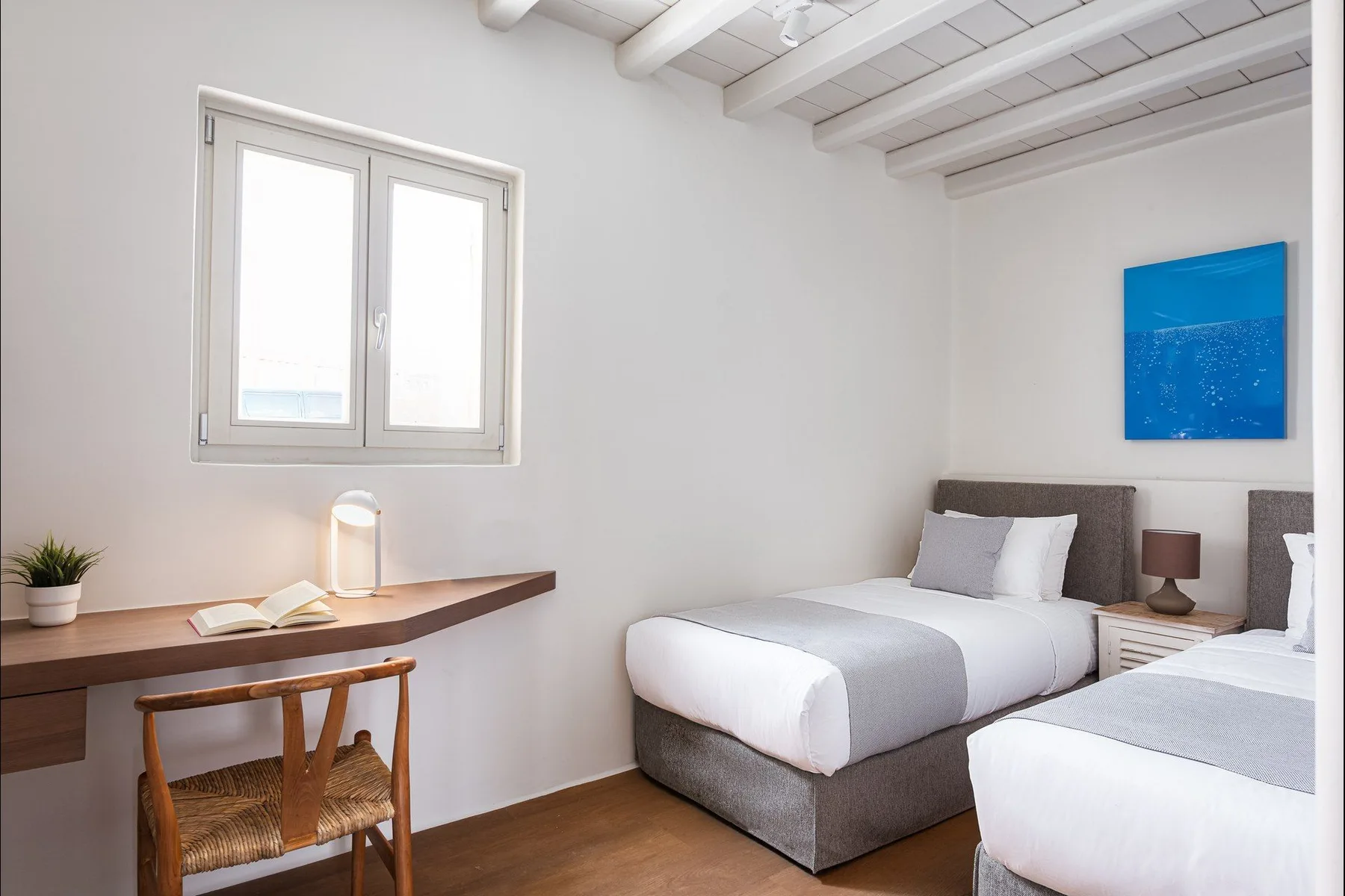 Un dormitorio luminoso con dos camas, un escritorio y arte azul en la pared.