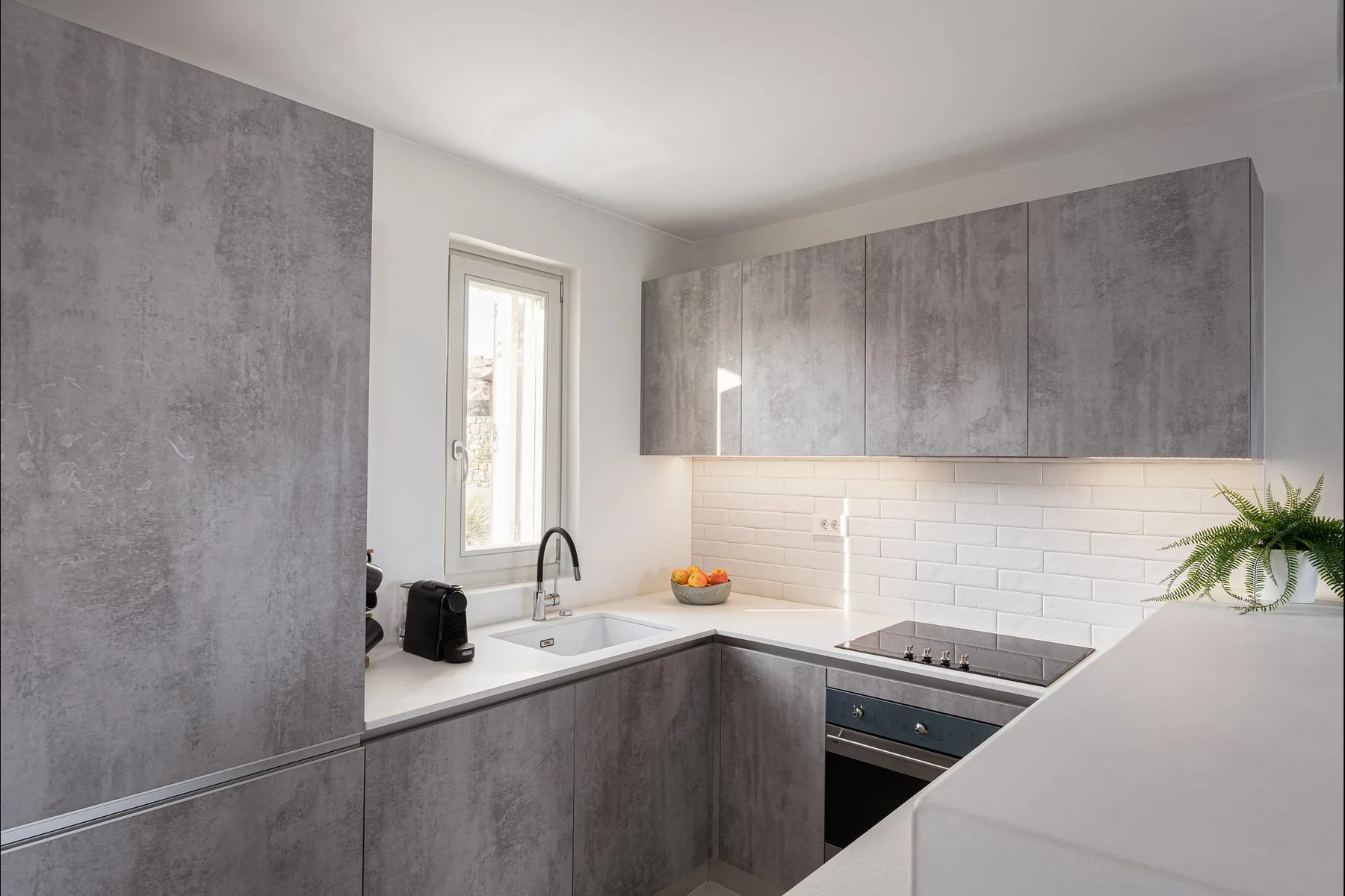 Una cocina moderna con gabinetes grises, encimeras blancas y un salpicadero de azulejos.