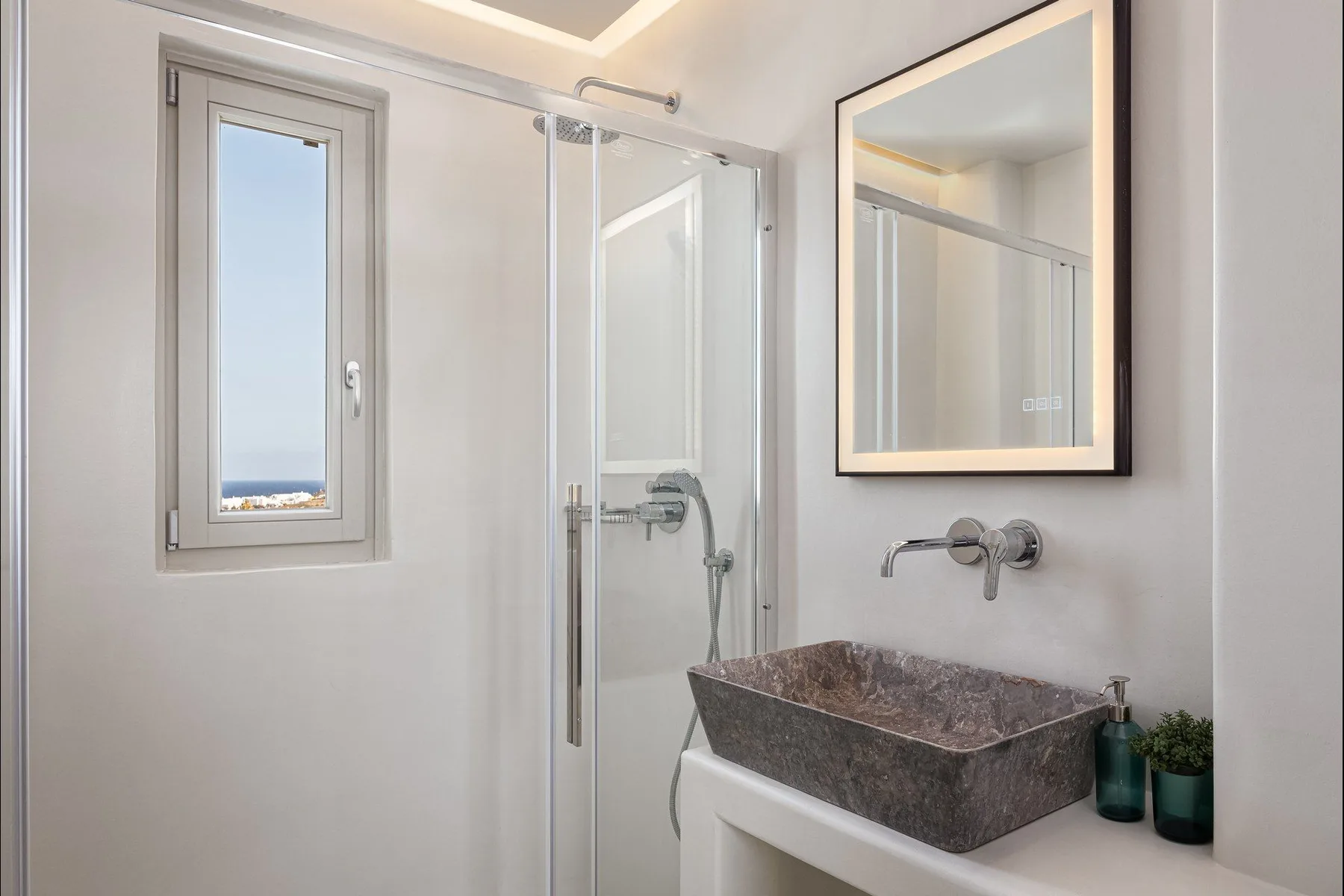 Un baño luminoso con lavabo de piedra, espejo de pared y ducha de cristal.