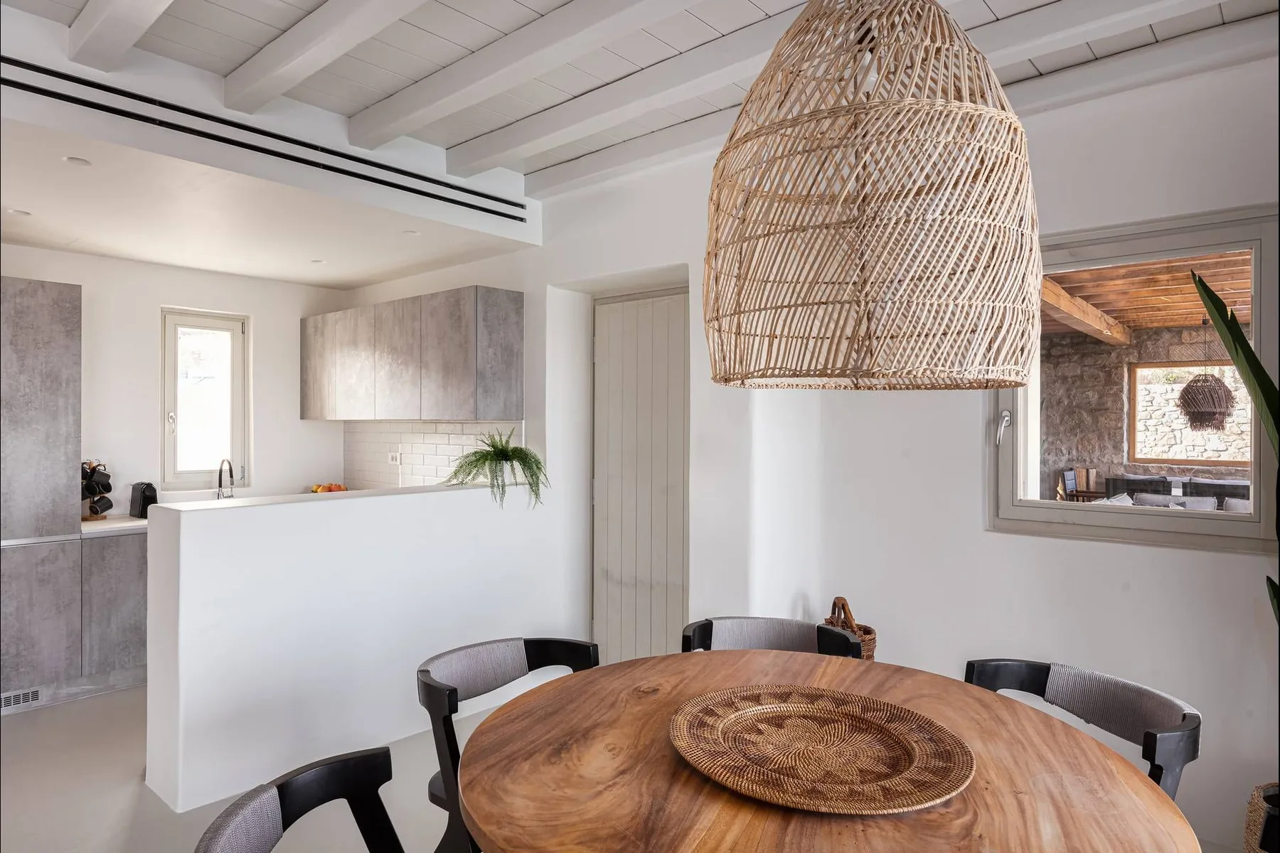 Comedor con una mesa redonda de madera bajo una lámpara colgante tejida.
