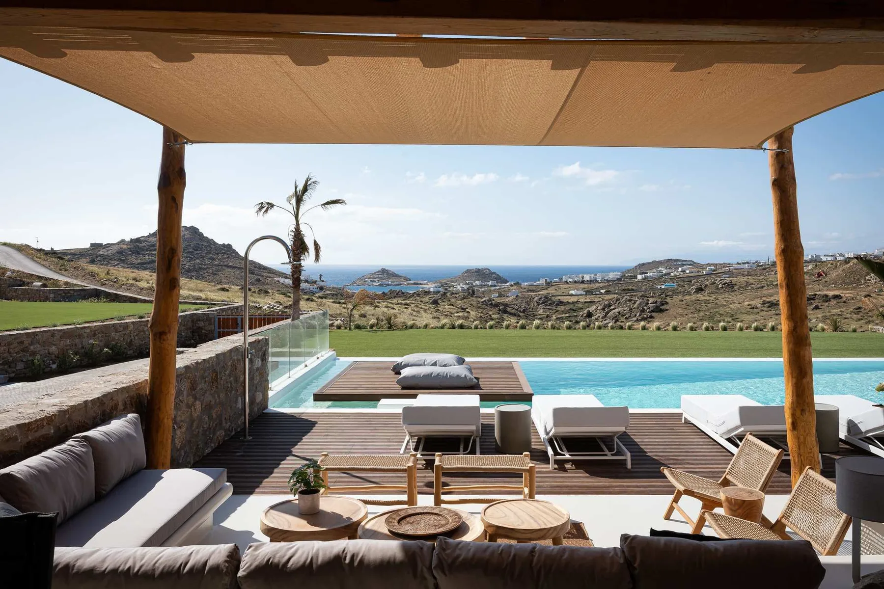 Un patio al aire libre da a una piscina, un césped y el mar a lo lejos.