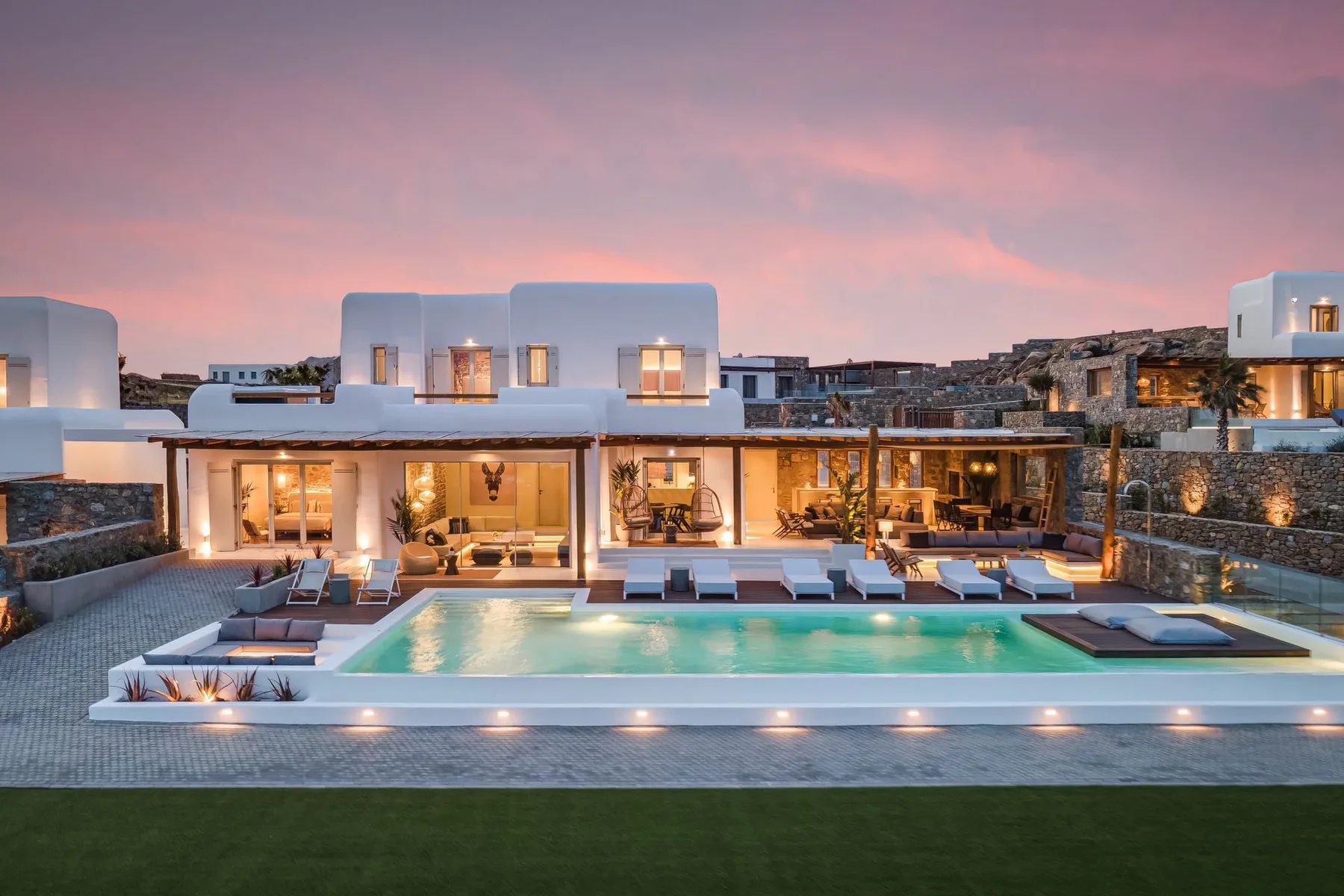 Una casa moderna da a una piscina y una zona de estar al aire libre al atardecer.