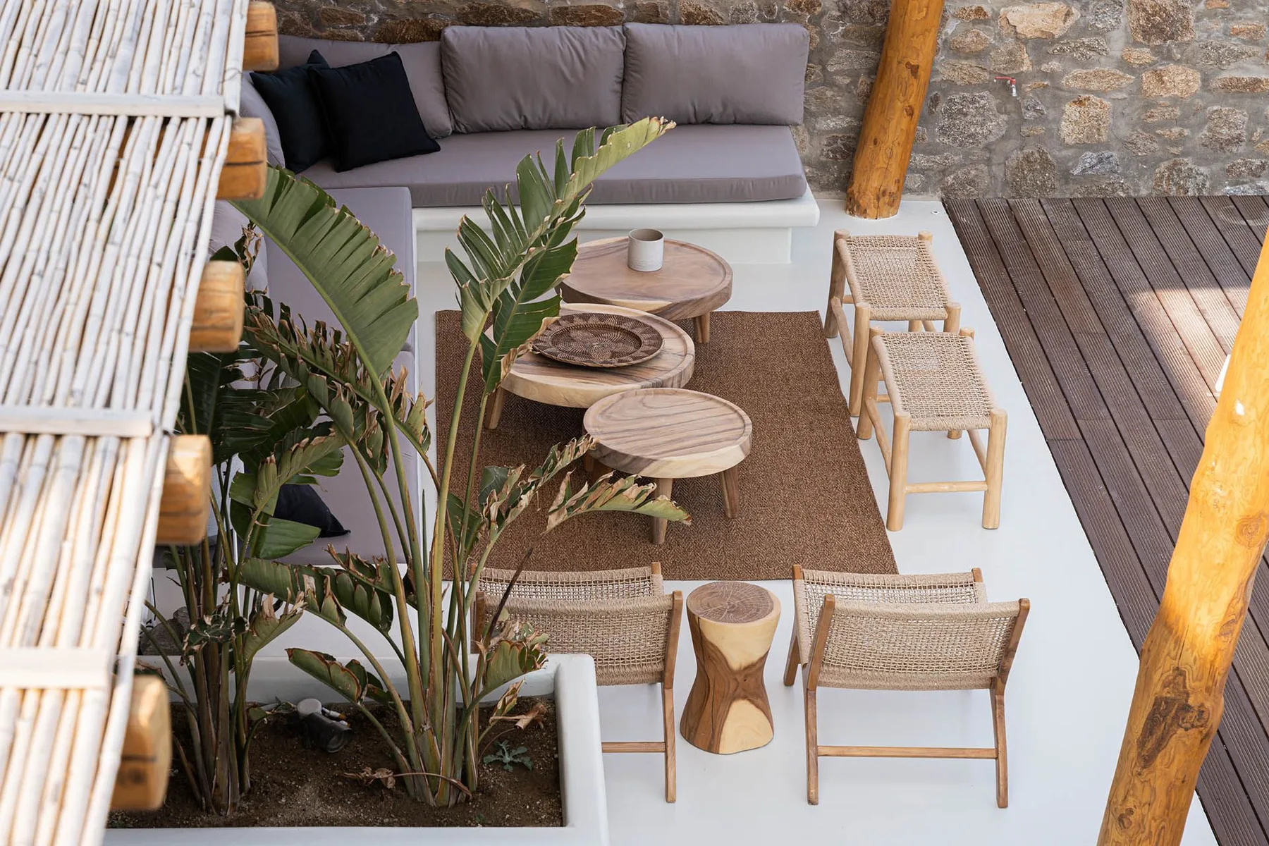 Una zona de estar al aire libre con asientos acolchados, sillas tejidas y mesas pequeñas.