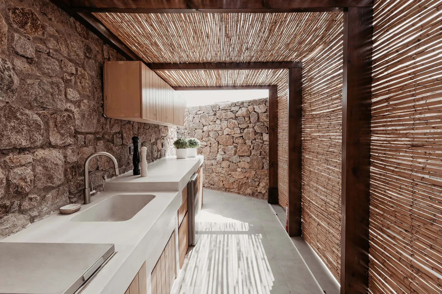 A modern outdoor kitchen with a long counter and woven screens.