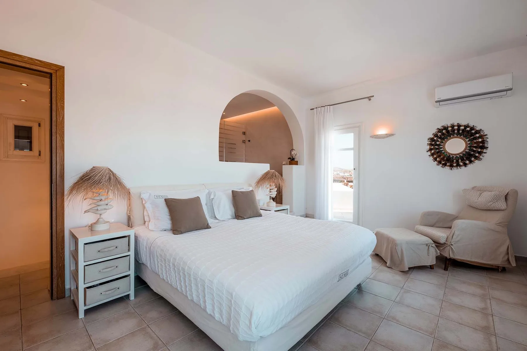 A bright bedroom with a large bed and an arched alcove.