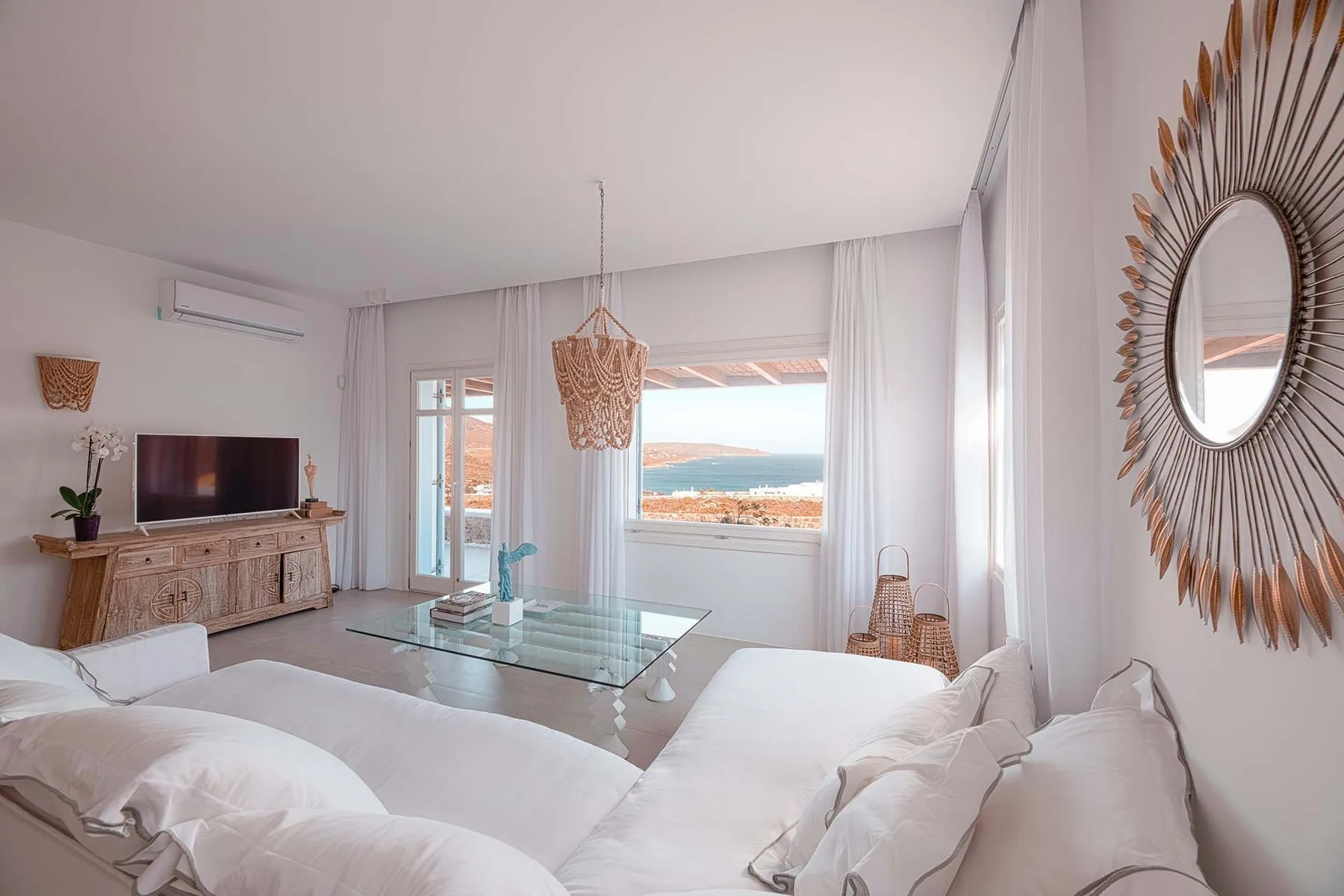 A bright living room with white seating and a wide window overlooking the sea.