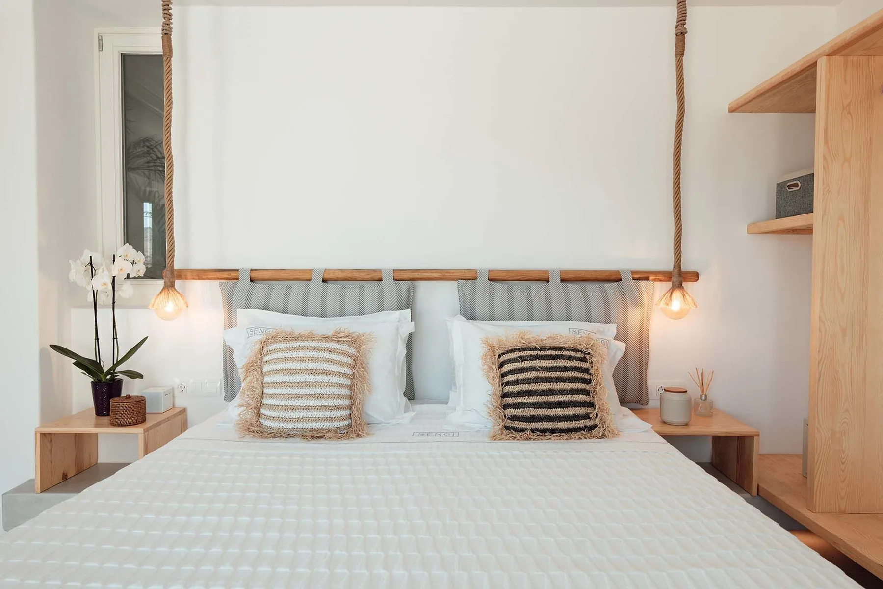 A bedroom with a neatly made bed and hanging pendant lights.