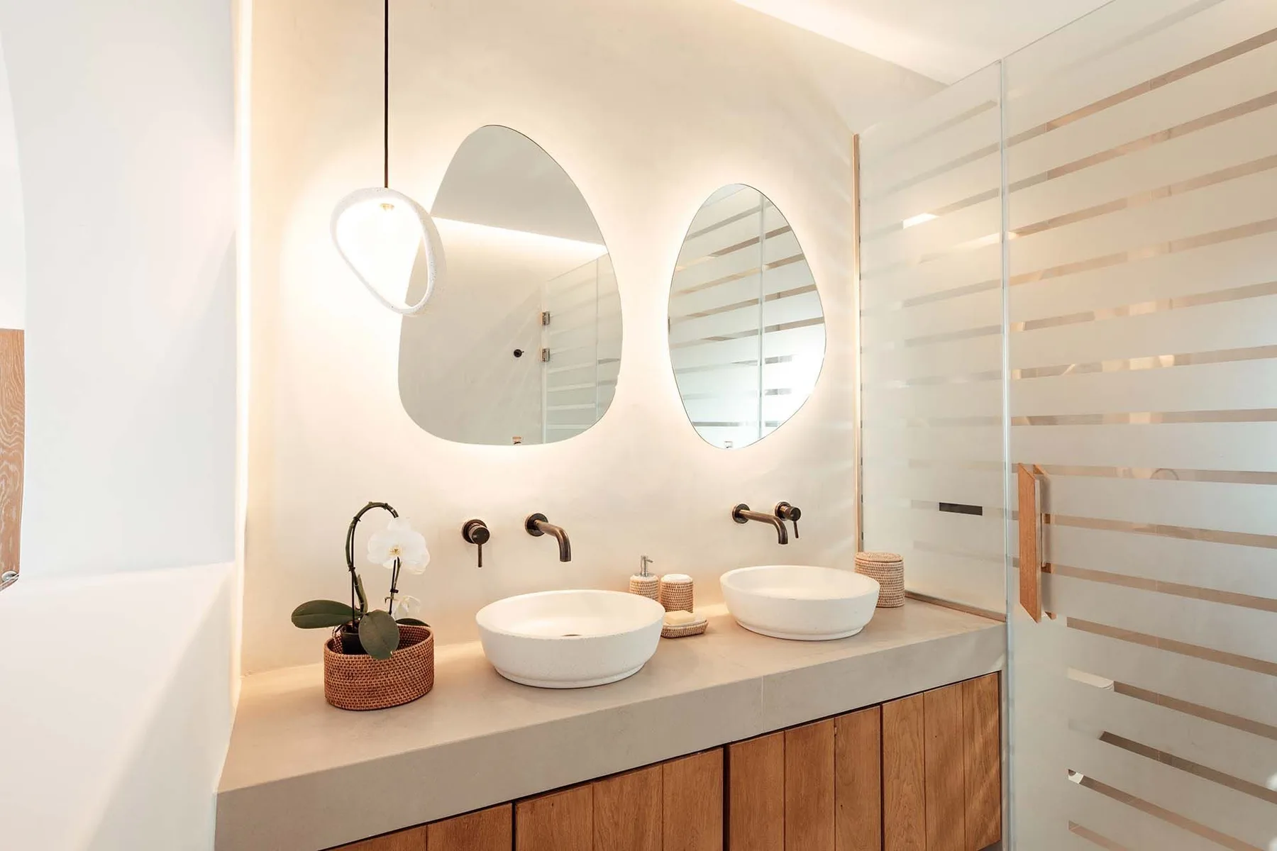 A bright bathroom vanity with two basins and mirrors beside a glass shower.