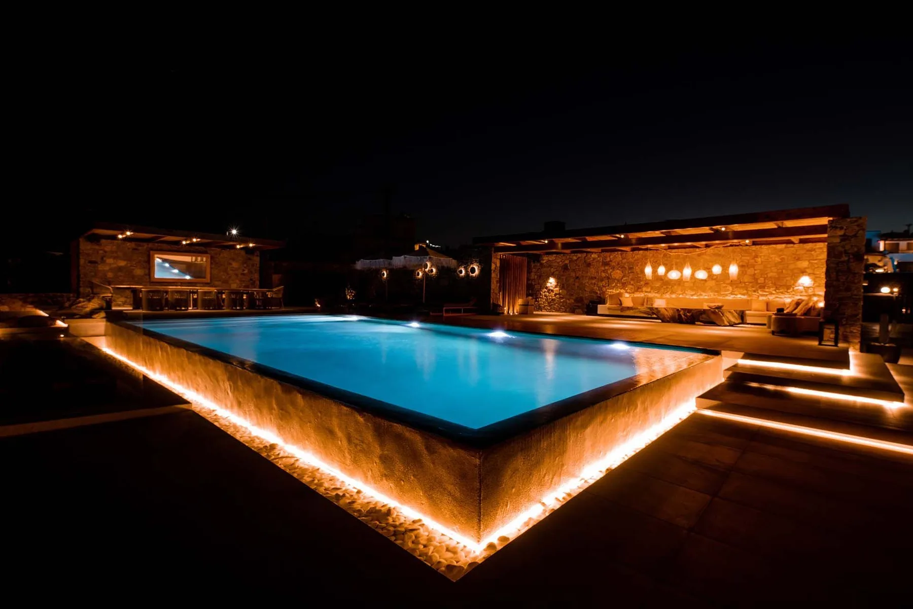 A lit outdoor pool at night beside a stone-clad building.