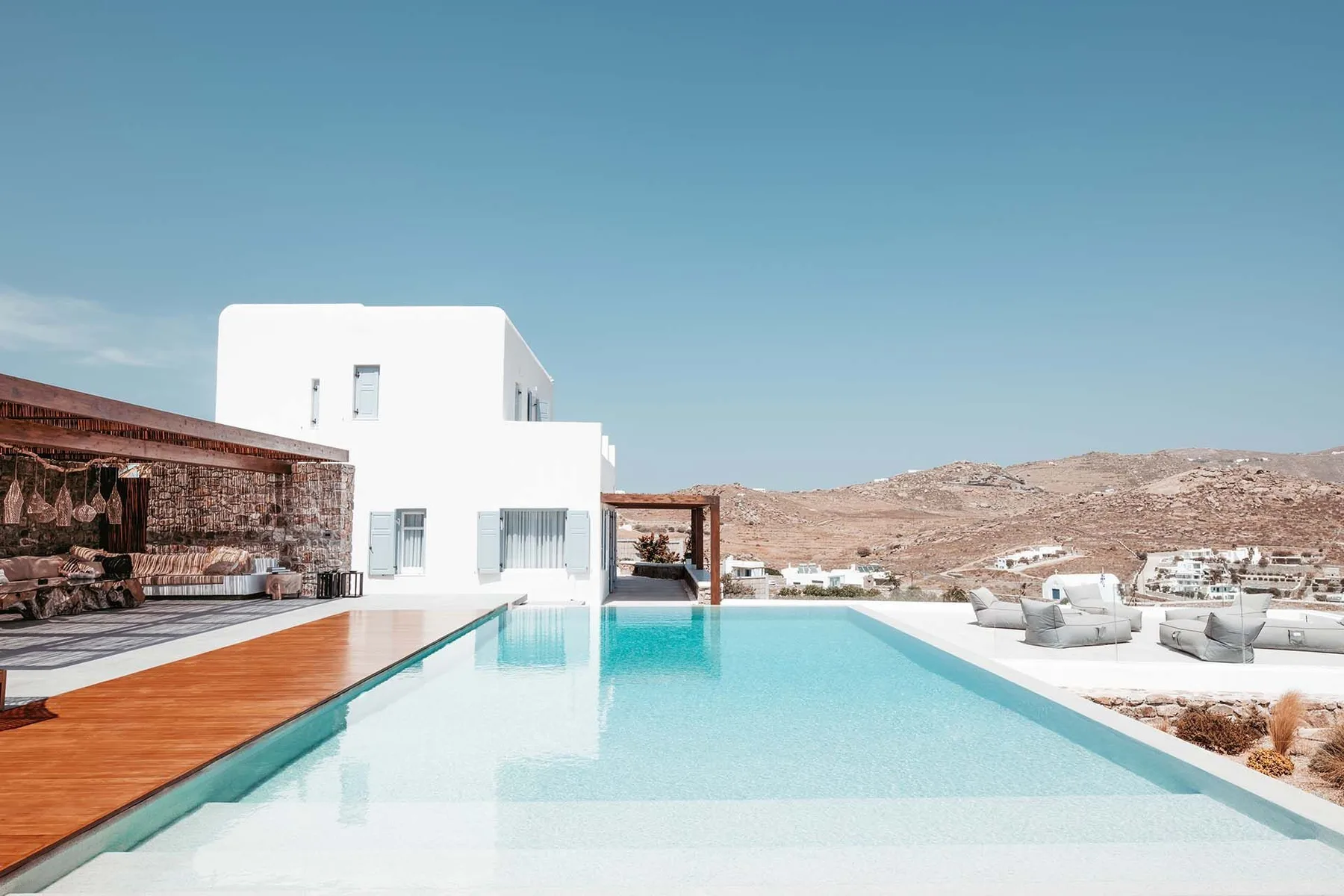 An outdoor swimming pool beside a white building, with a wooden deck and dry hills beyond.