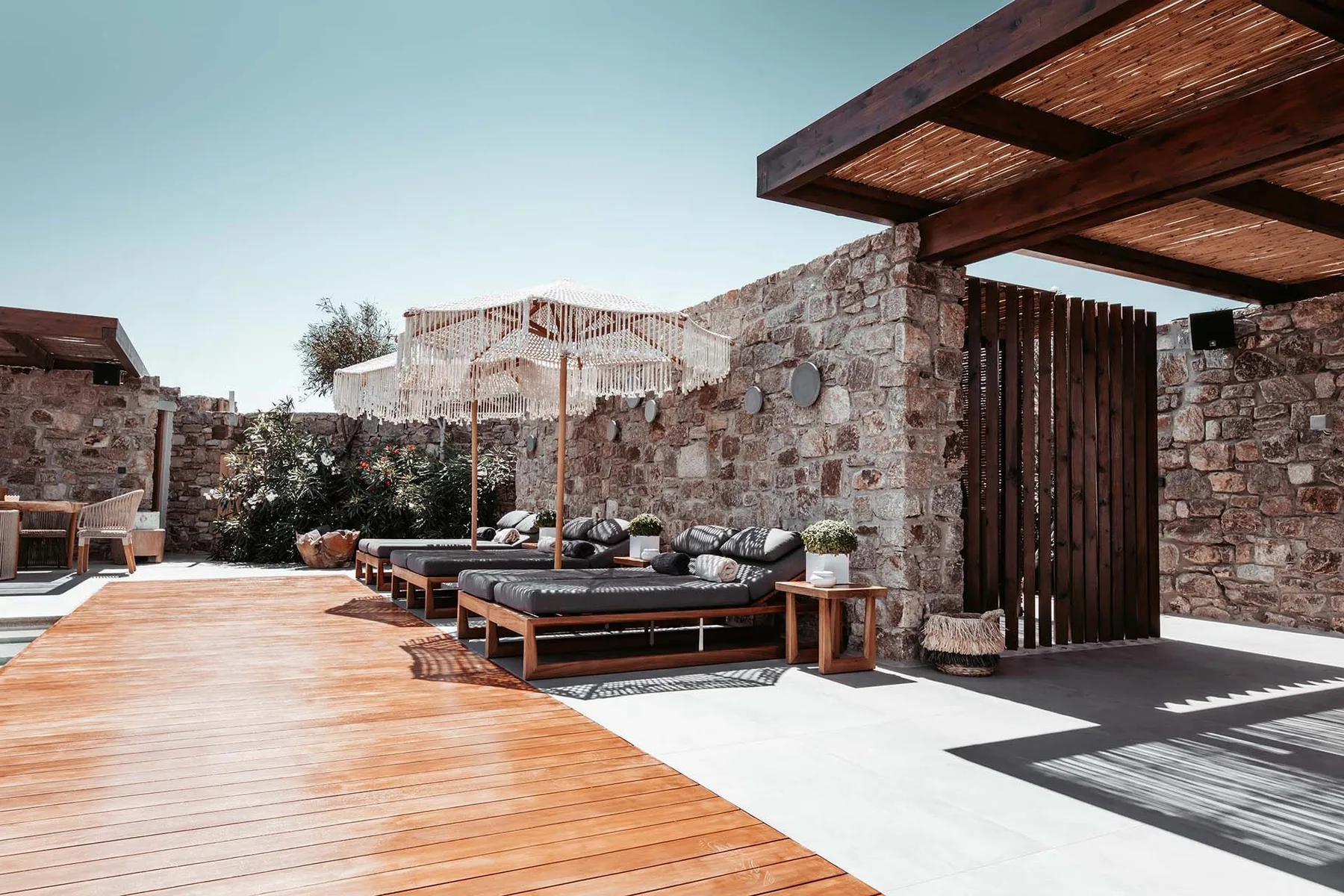A stone-walled outdoor lounge with cushioned seating and a wooden deck.