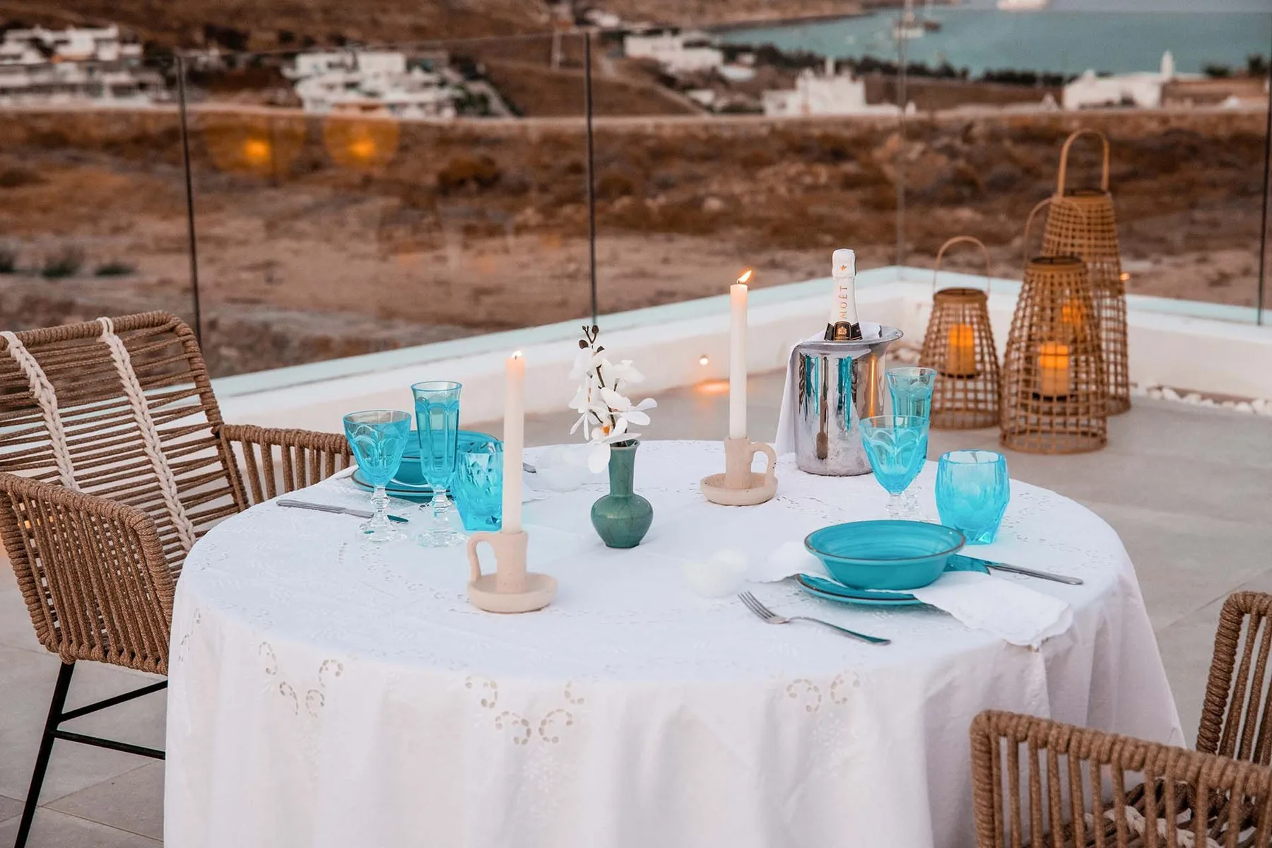 A rooftop dining table is set with turquoise glassware and candles.