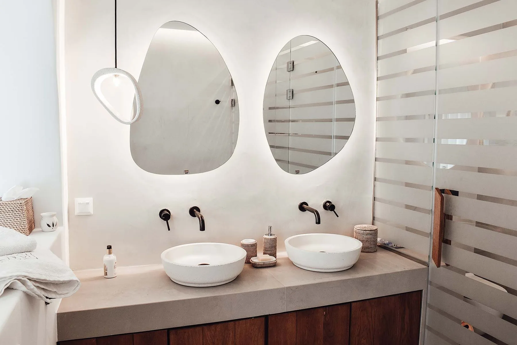A bathroom vanity with two vessel sinks and oval mirrors.