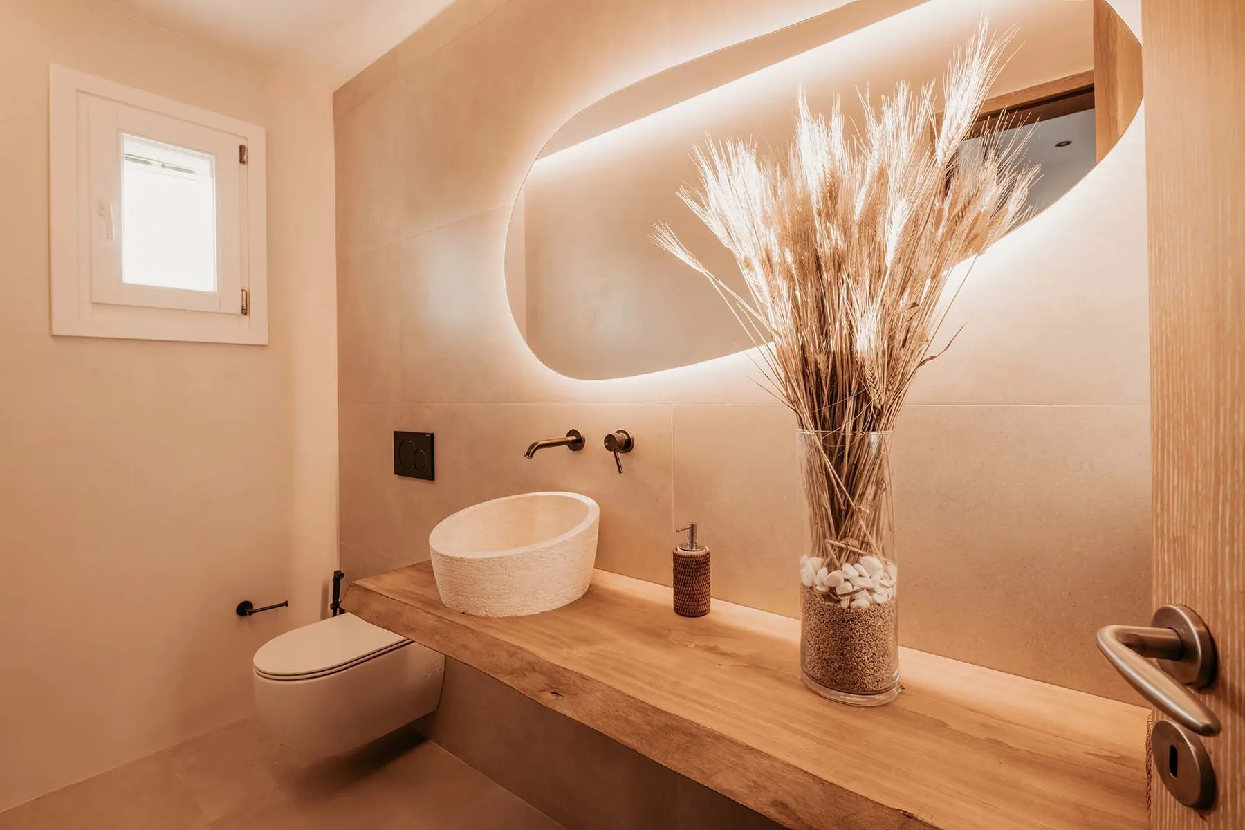 A warm-toned bathroom with a vessel sink beneath a backlit mirror.